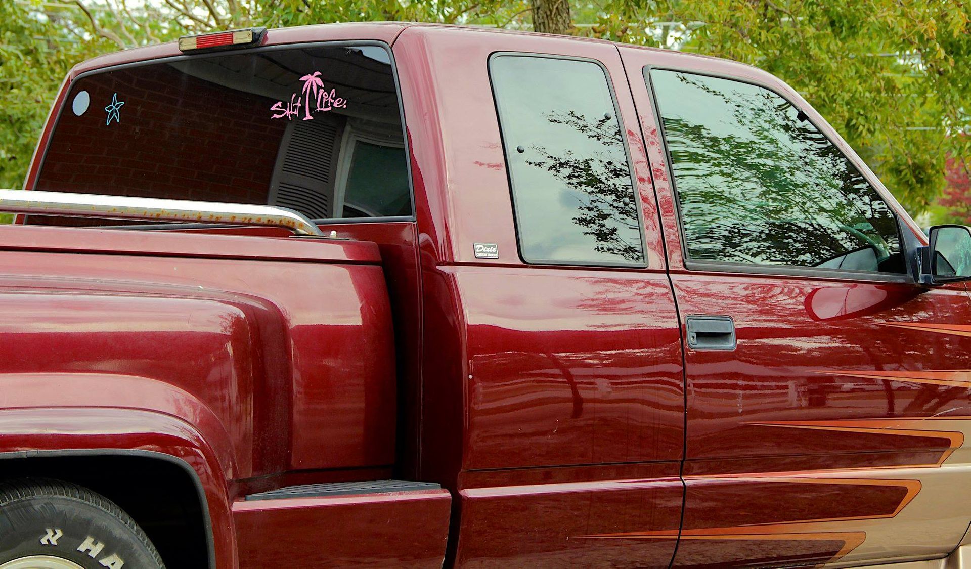 A side view of a maroon pickup truck parked outdoors, featuring tinted windows and a silver roll bar on the truck bed.