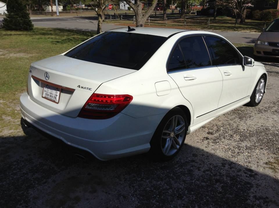 A white Mercedes-Benz C-Class sedan parked on a gravel driveway in a grassy, residential area.