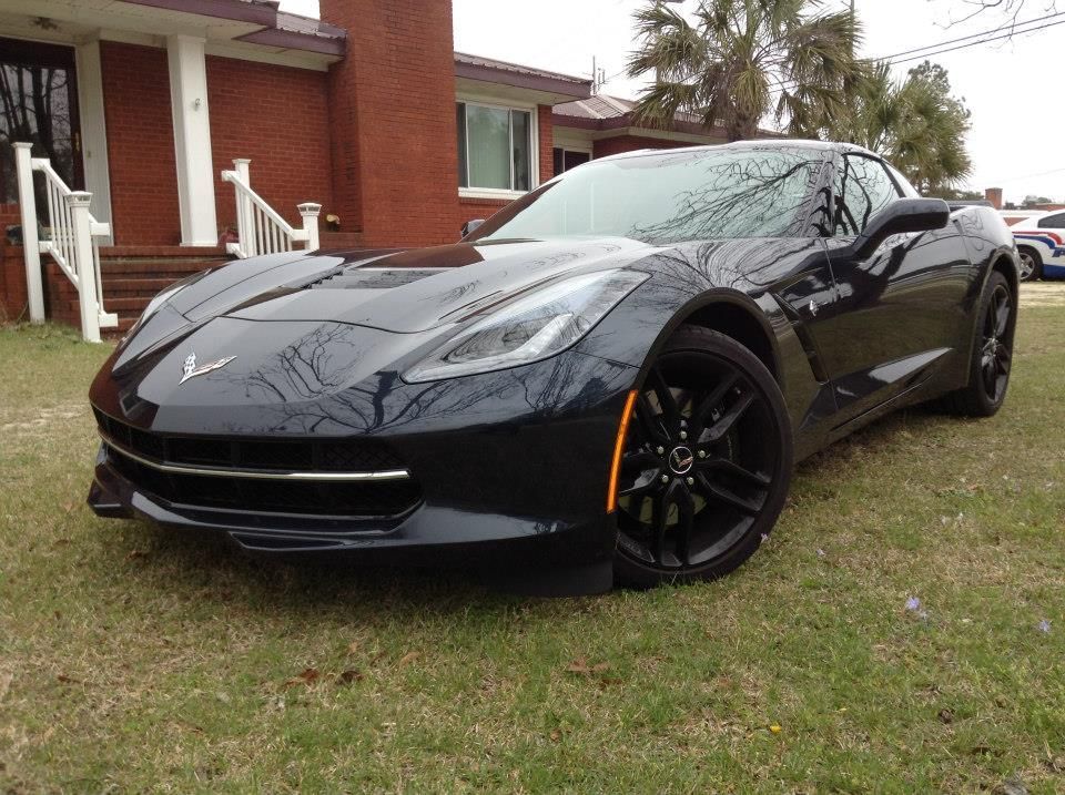 A black Chevrolet Corvette parked on a residential lawn in front of a brick house.
