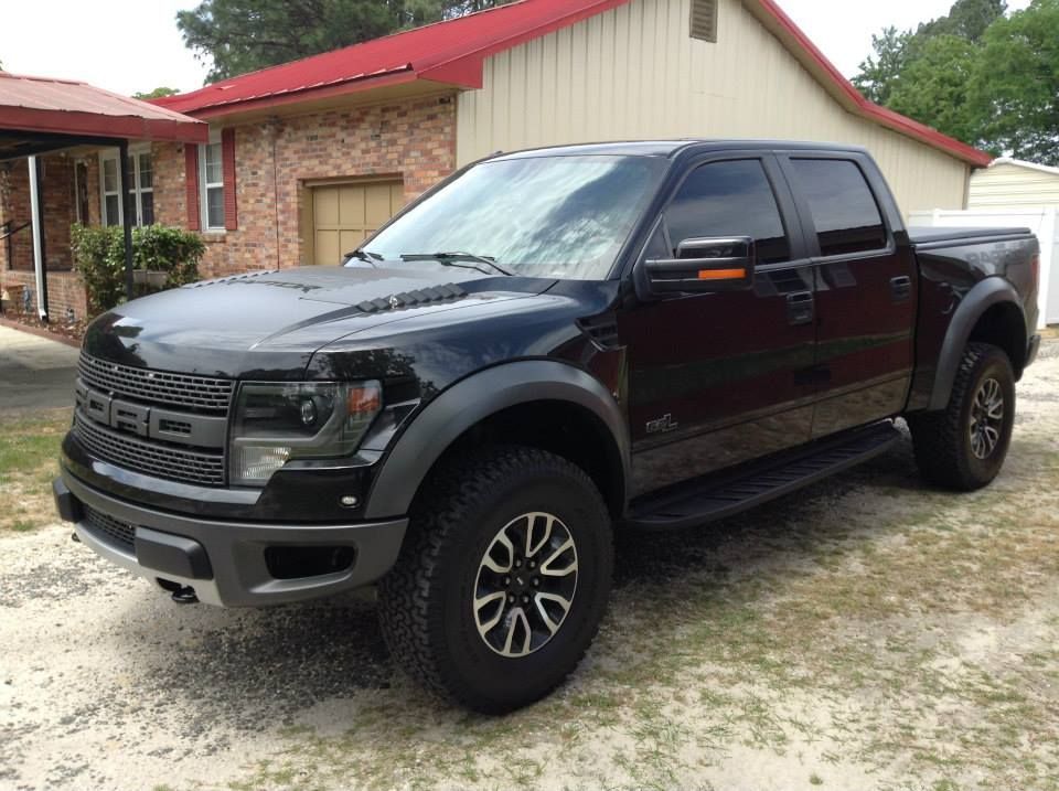 A black Ford F-150 Raptor truck parked in front of a brick house with a red metal roof.