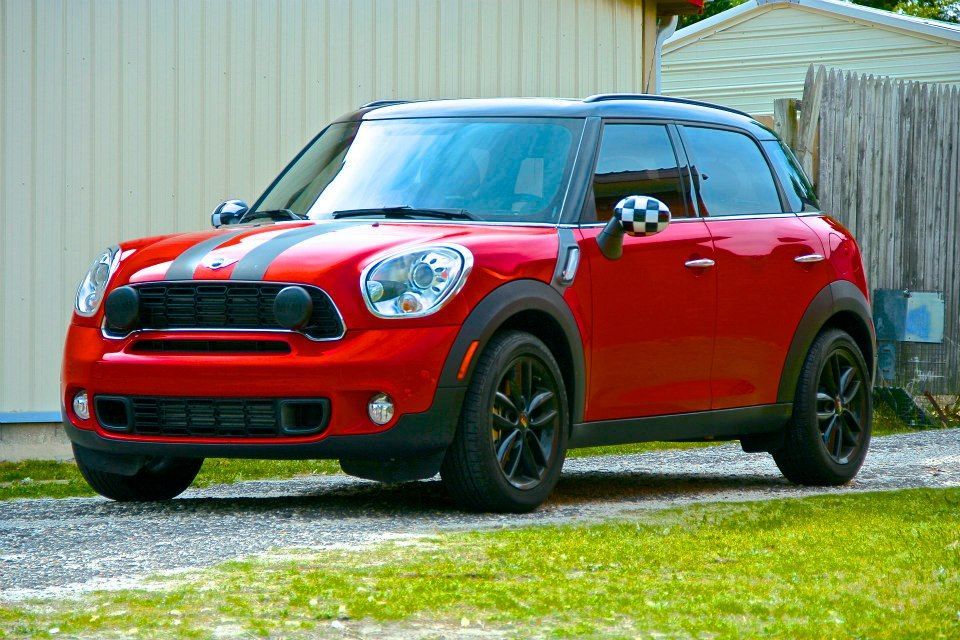 A red Mini Cooper Countryman parked on a gravel driveway next to a white building.