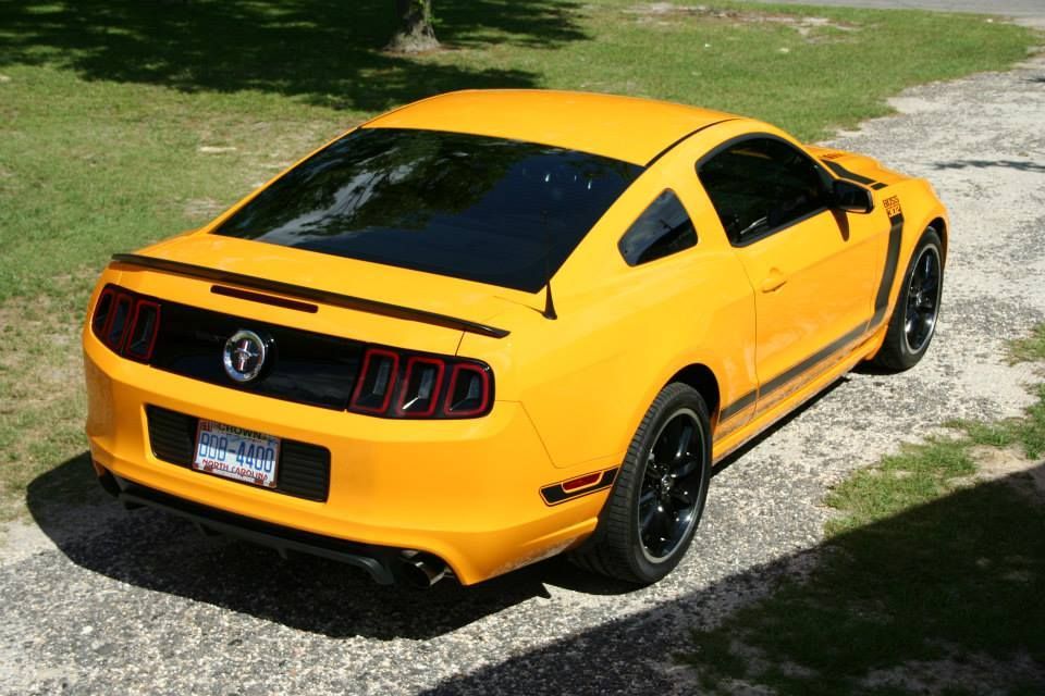 A bright yellow Ford Mustang coupe parked on a gravel driveway, viewed from the rear three-quarter angle.