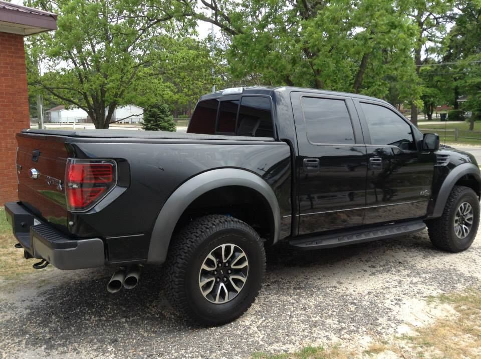 A black Ford F-150 crew cab pickup truck parked on a gravel lot next to a brick building.