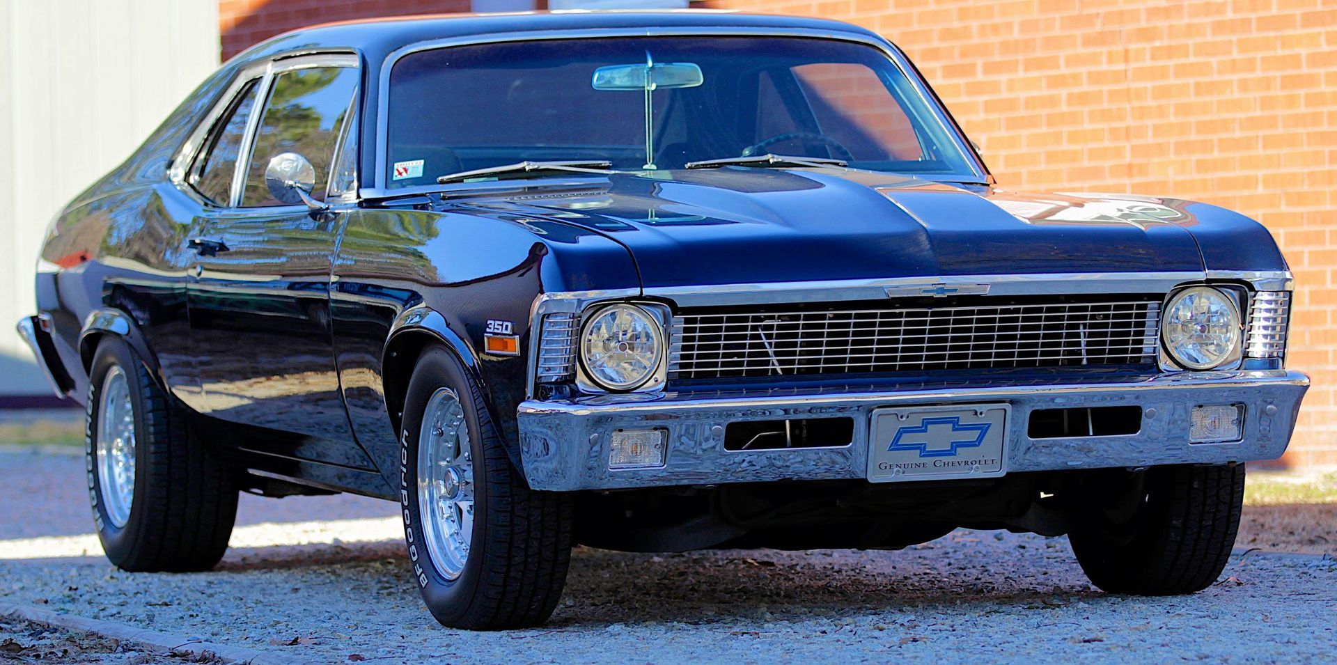 A shiny, dark blue 1970s Chevrolet Nova muscle car parked on a gravel surface.