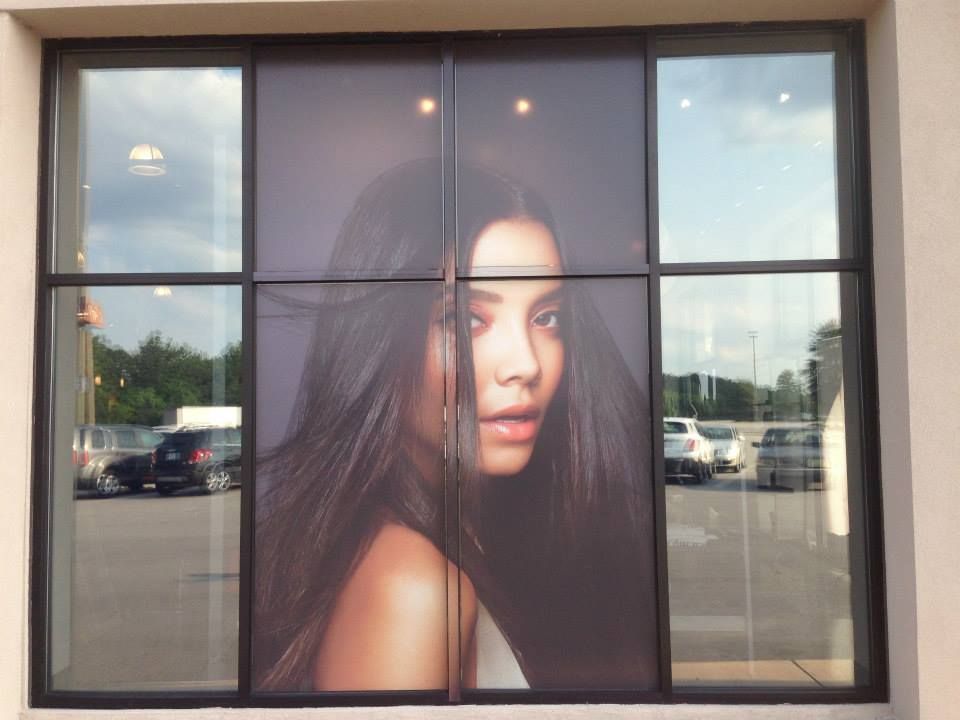 Window decal of a woman with long dark hair, displayed on a paneled glass storefront window with a parking lot in back.