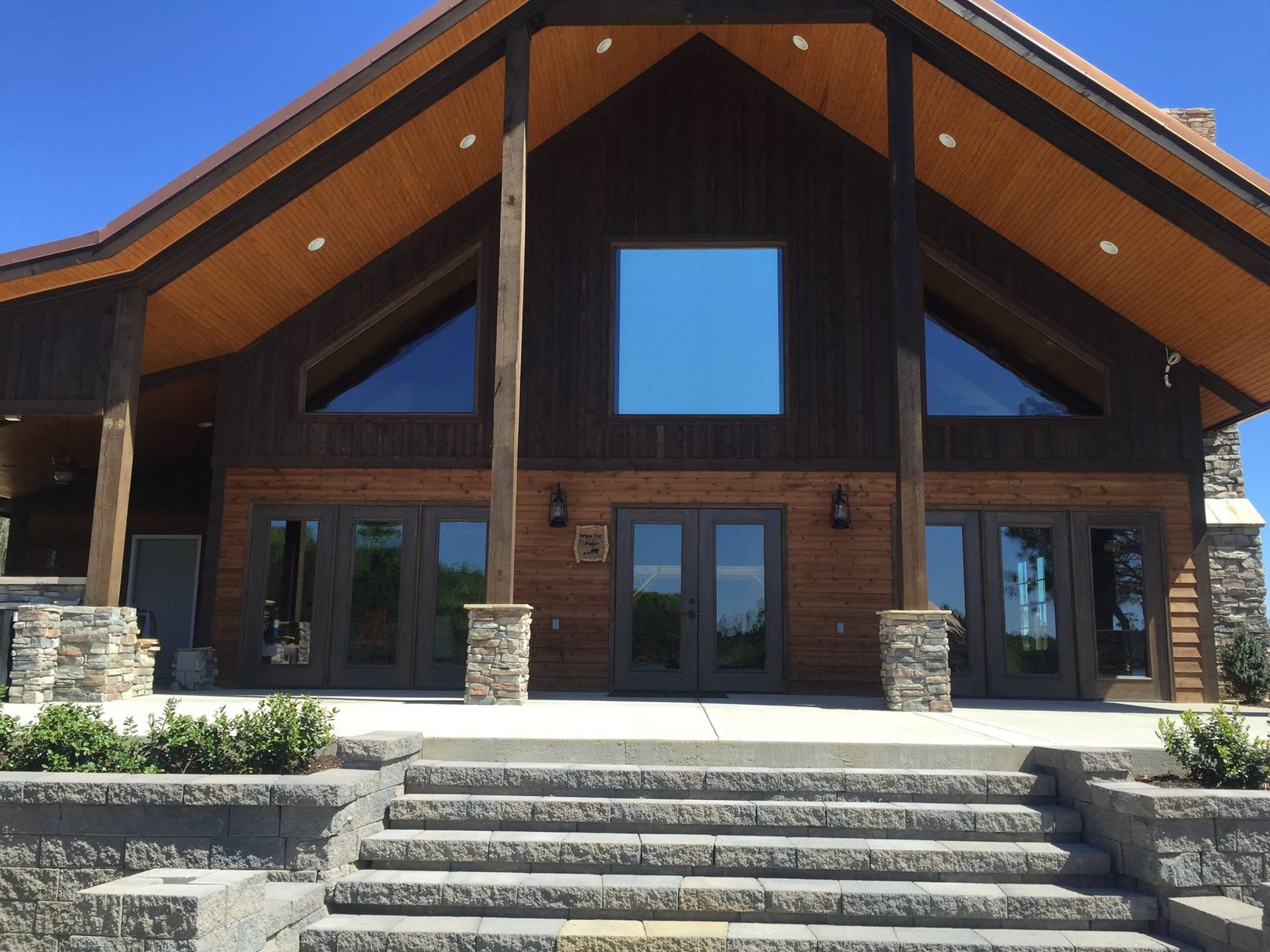 A rustic building with dark wood siding, stone pillar bases, and a large central window above glass double doors.