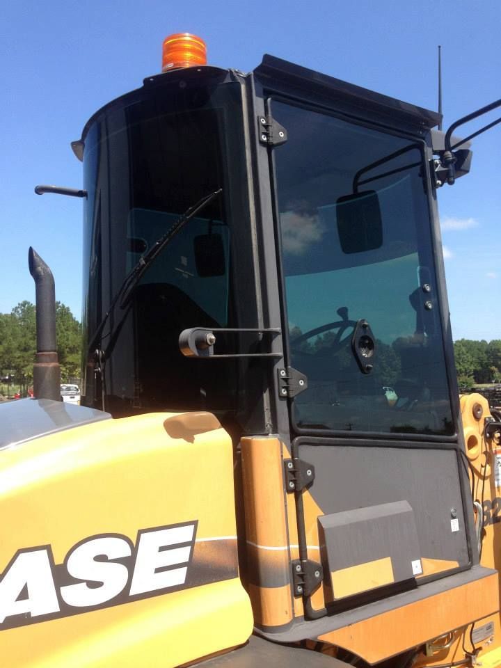The yellow cab and door of a Case construction vehicle, featuring tinted windows and an orange warning beacon on top.