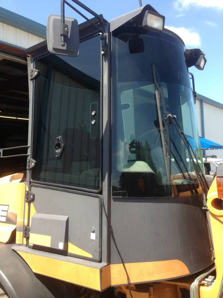 A close-up view of the yellow cab of a construction vehicle, showing the windshield, door, and exterior side mirror.