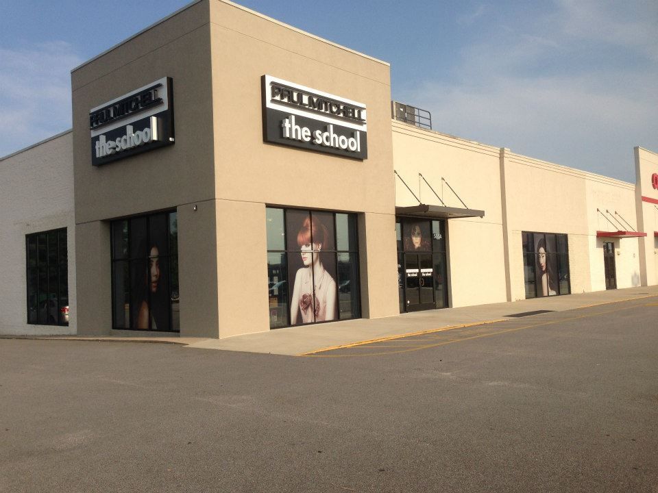 Exterior view of a Paul Mitchell The School building with a beige facade and large glass windows in a parking lot.