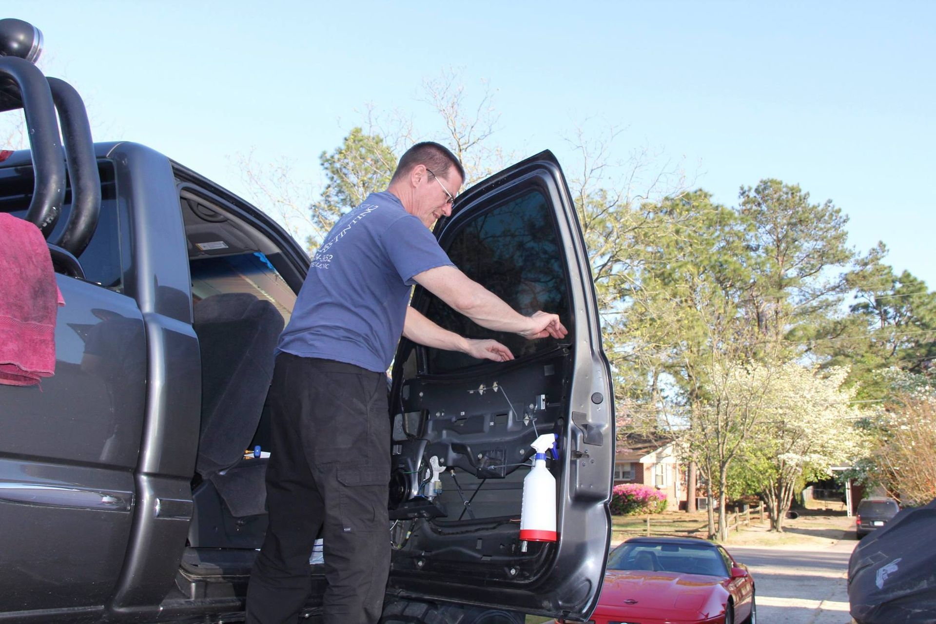 A person working on the inner mechanism of a grey truck door, with a spray bottle attached to the door frame.