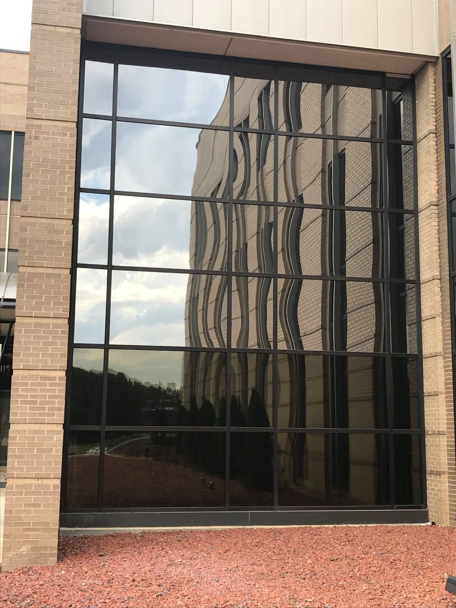A large grid of rectangular glass windows on a brick building, reflecting the surrounding landscape and sky.
