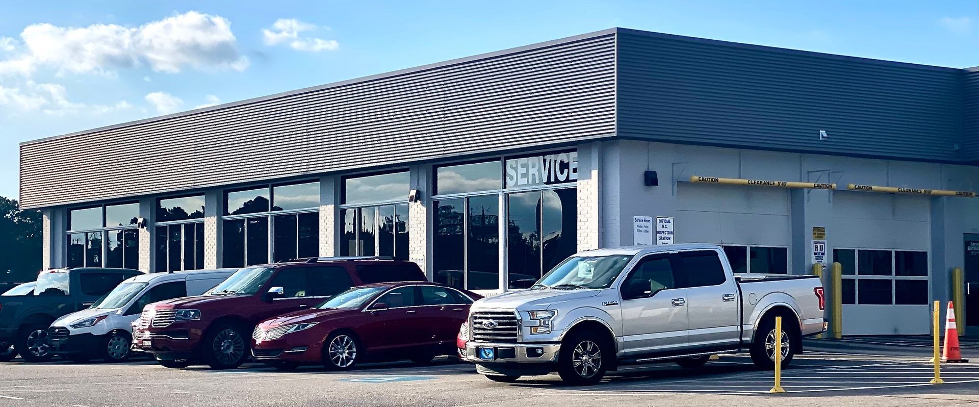 A single-story automotive service building with a dark metal awning, glass storefront, and parked vehicles outside.