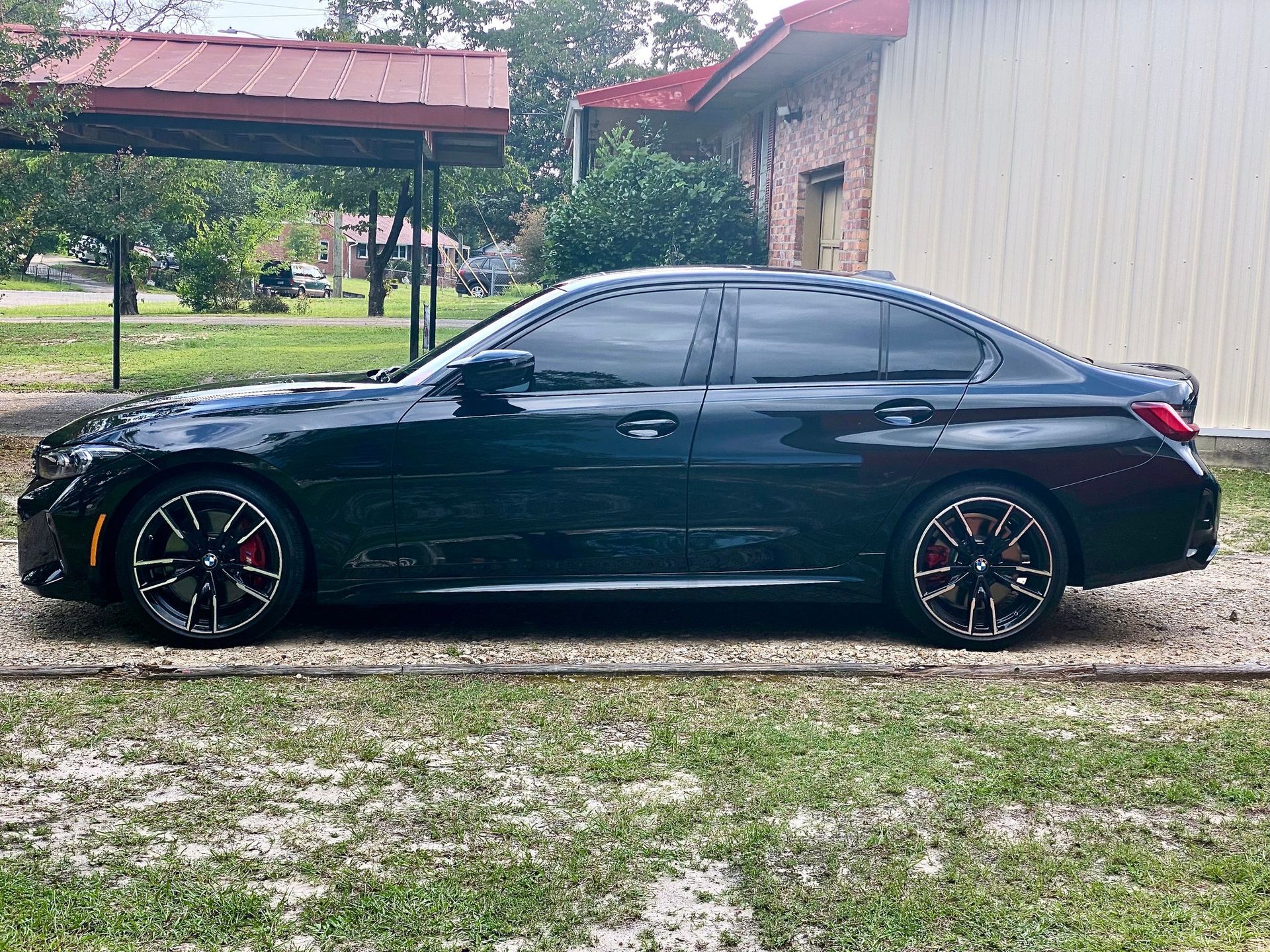 A black BMW sedan parked on a gravel driveway next to a building with a metal carport.