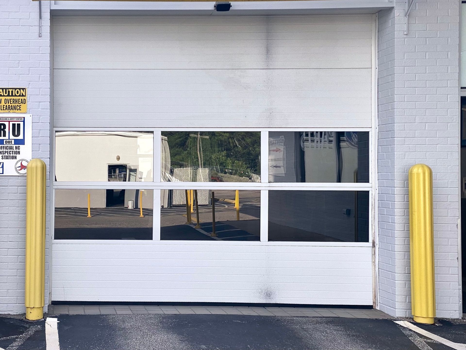 A white garage door with a central row of windows, flanked by two yellow bollards on a brick building exterior.