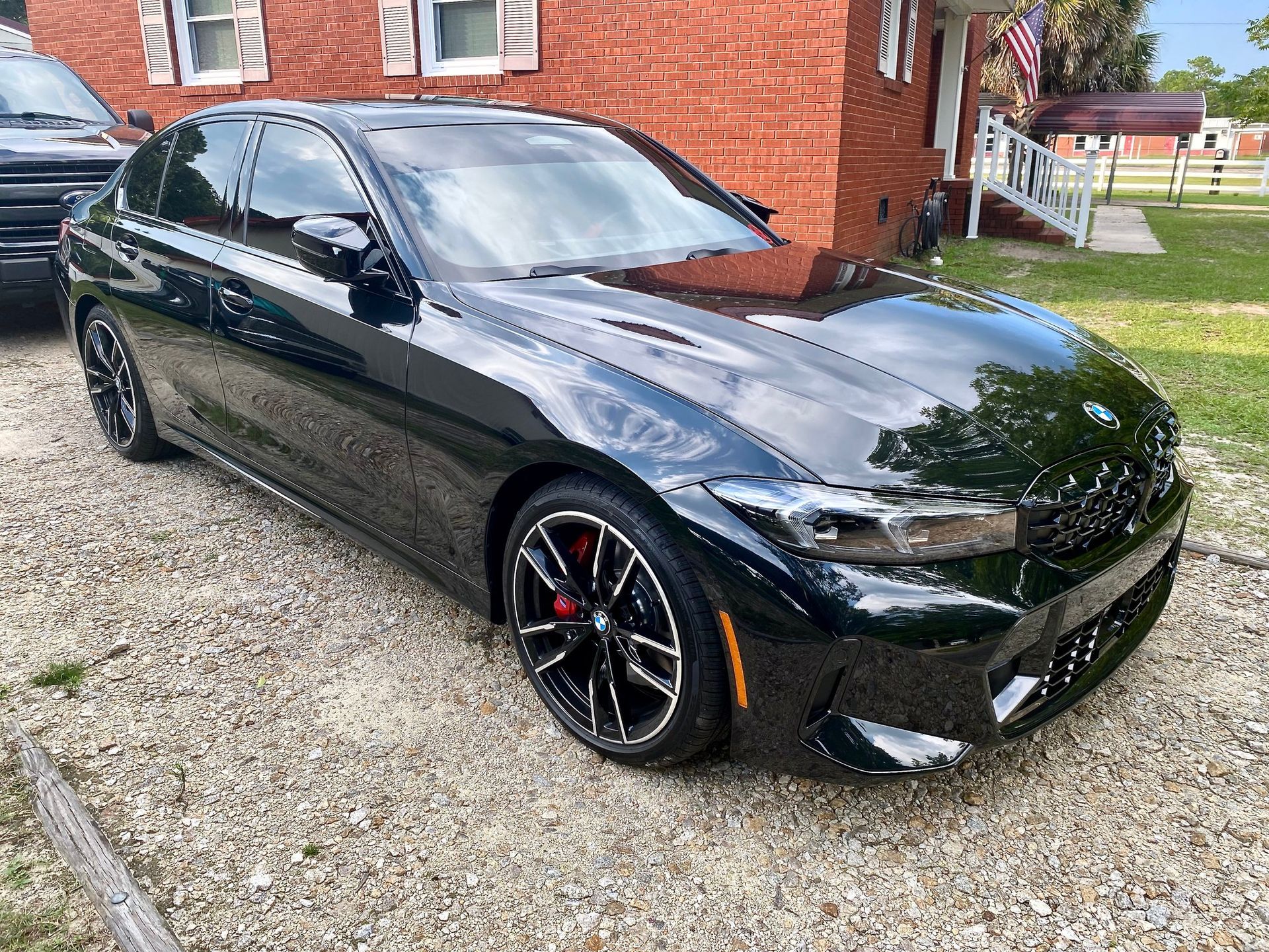 A black BMW sedan parked on a gravel driveway in front of a red brick house.