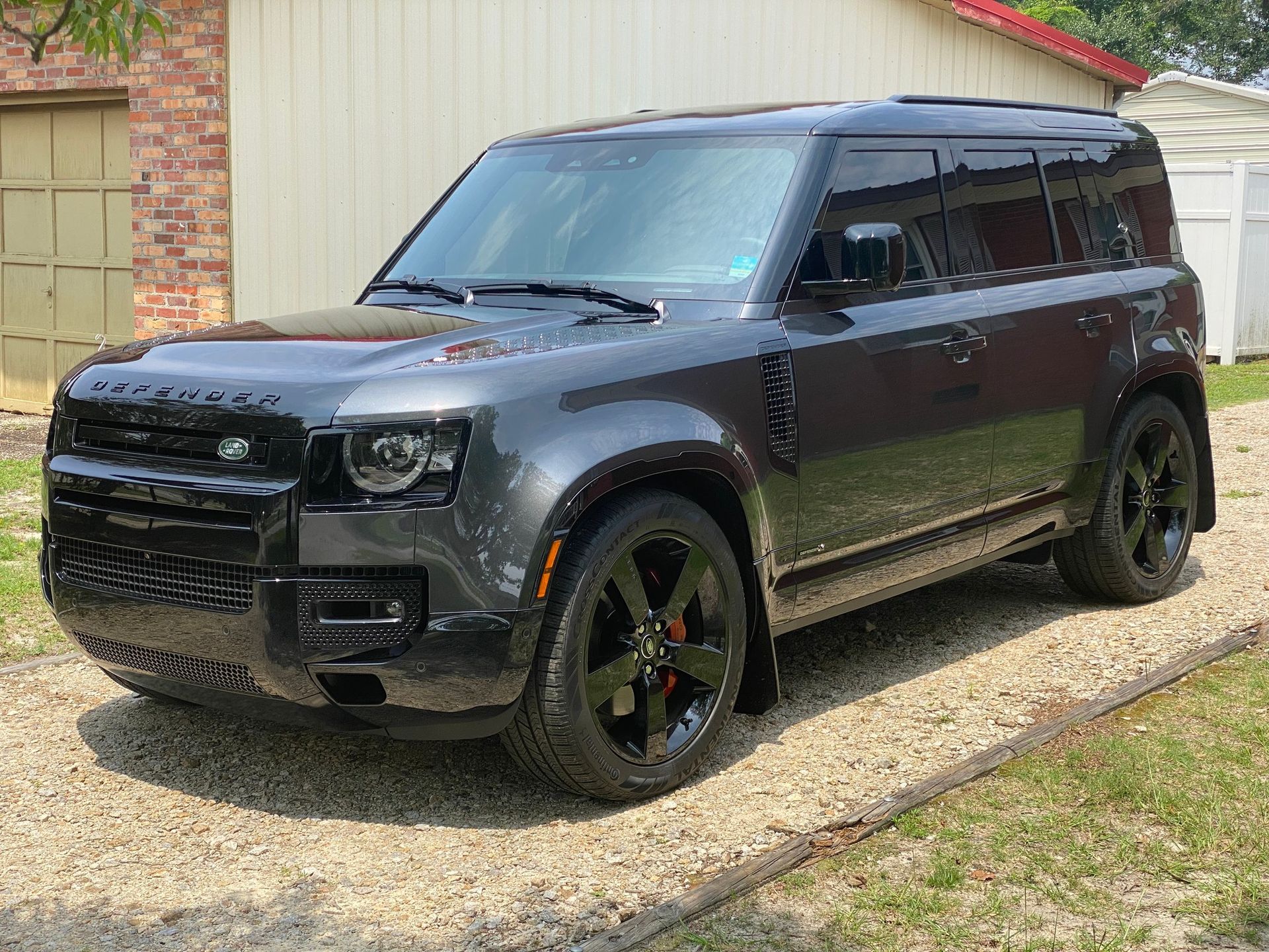 A dark gray Land Rover Defender SUV parked on a gravel driveway next to a brick building.