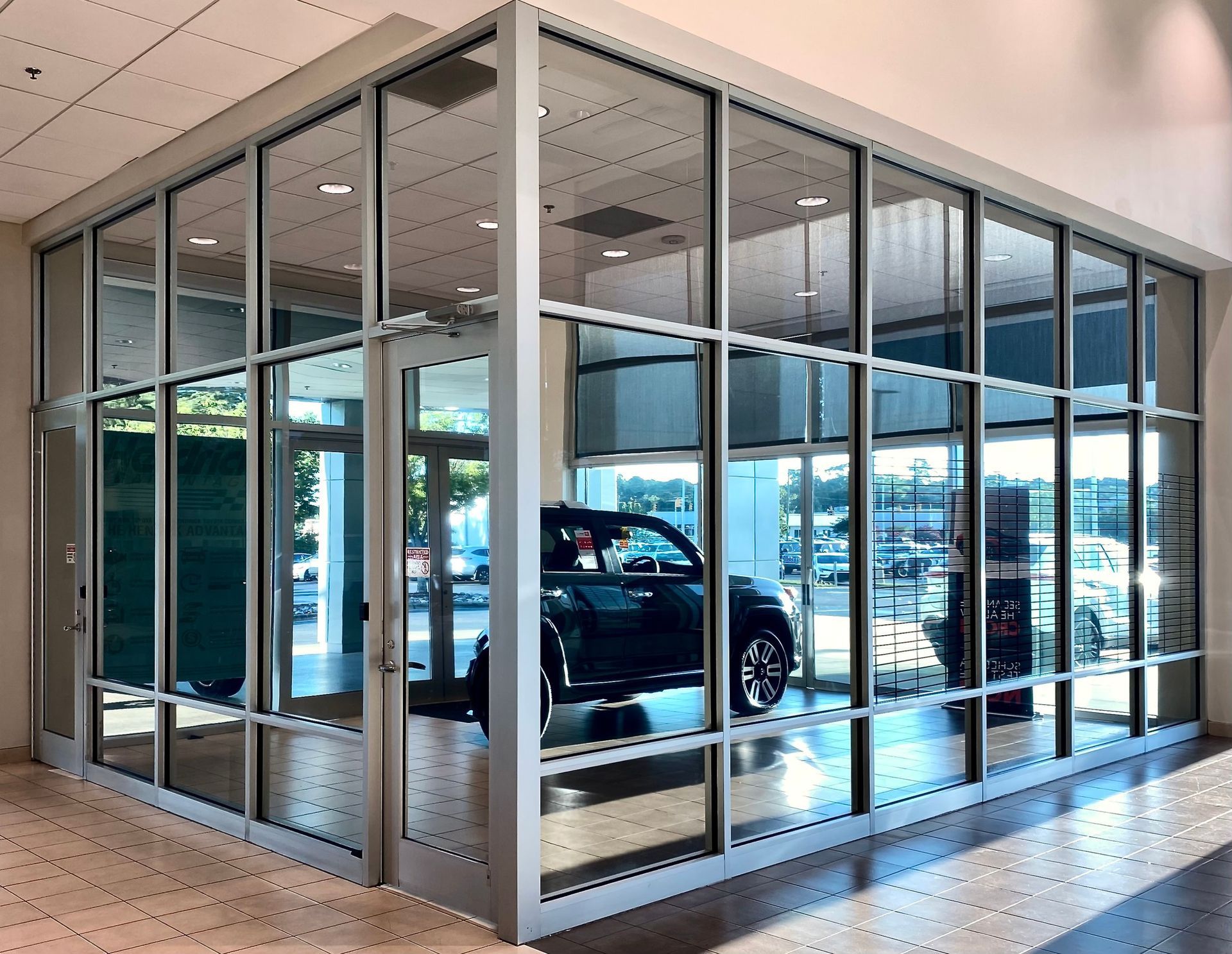 A row of cars parked outside a commercial building with large glass windows and a prominent corrugated metal roof.