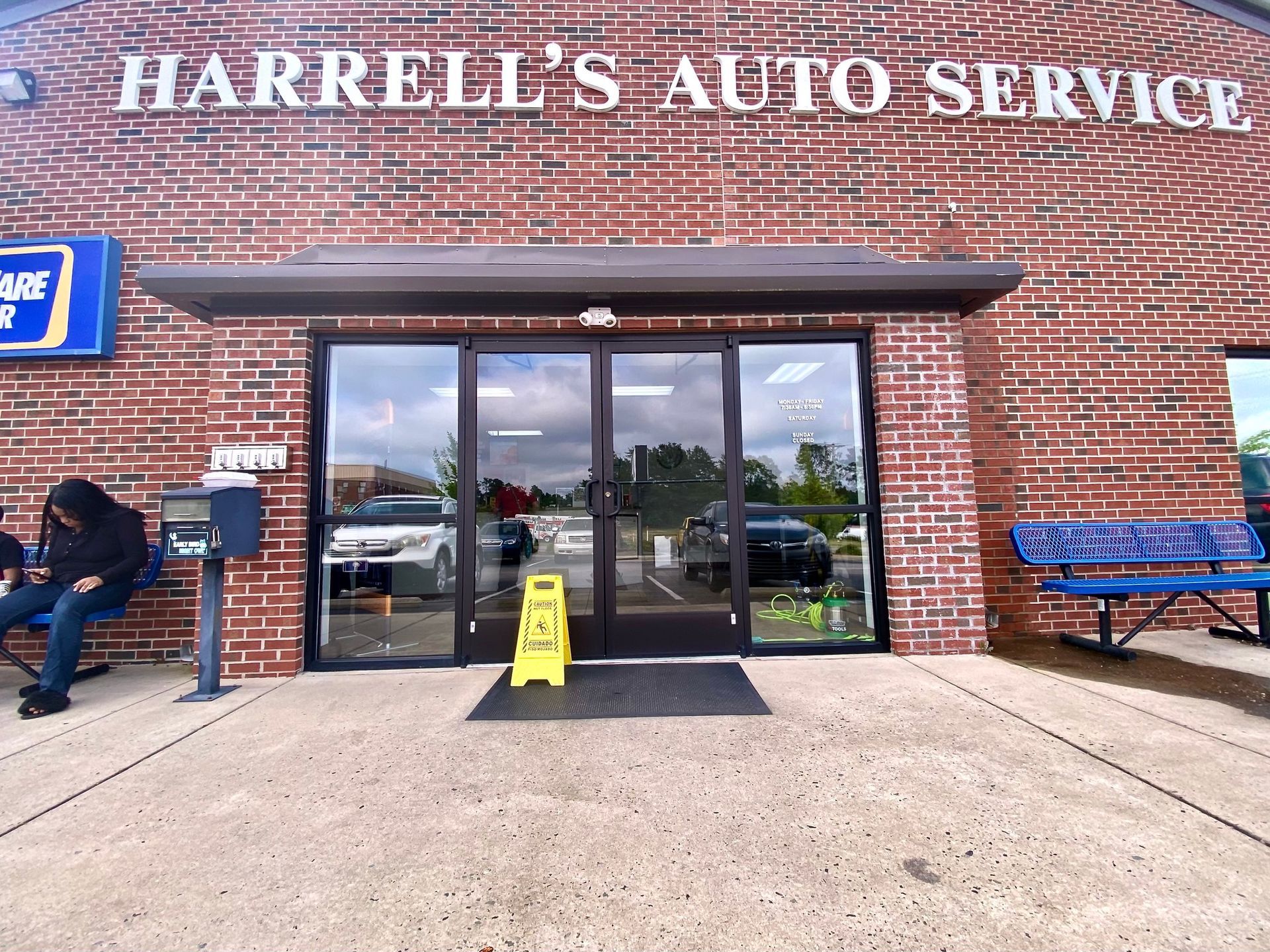 The exterior of Harrell's Auto Service, featuring a brick facade, glass entrance doors, and a yellow caution floor sign.