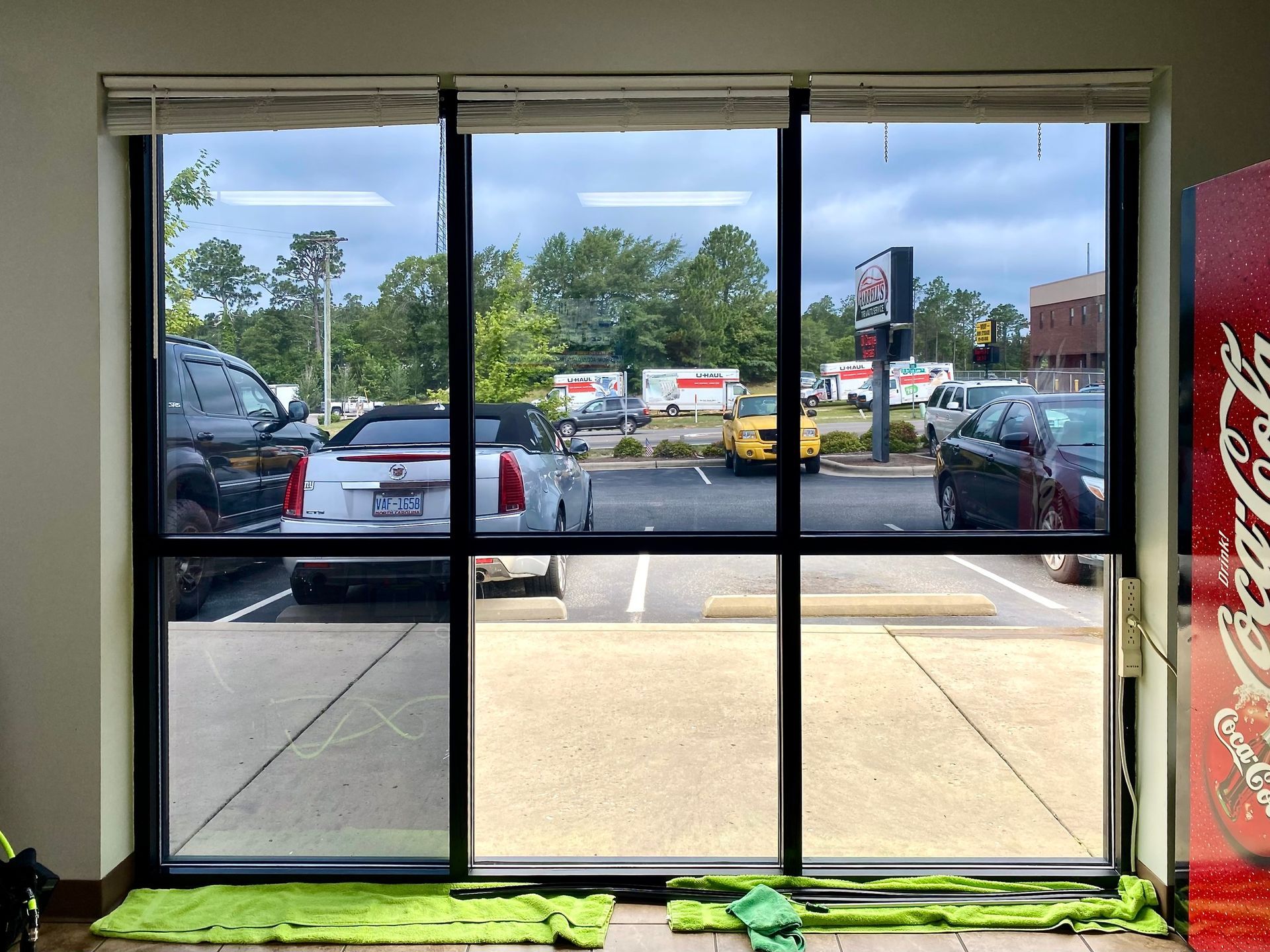 Large window with tinted glass showing a parking lot with cars and a Coca-Cola vending machine on the right.