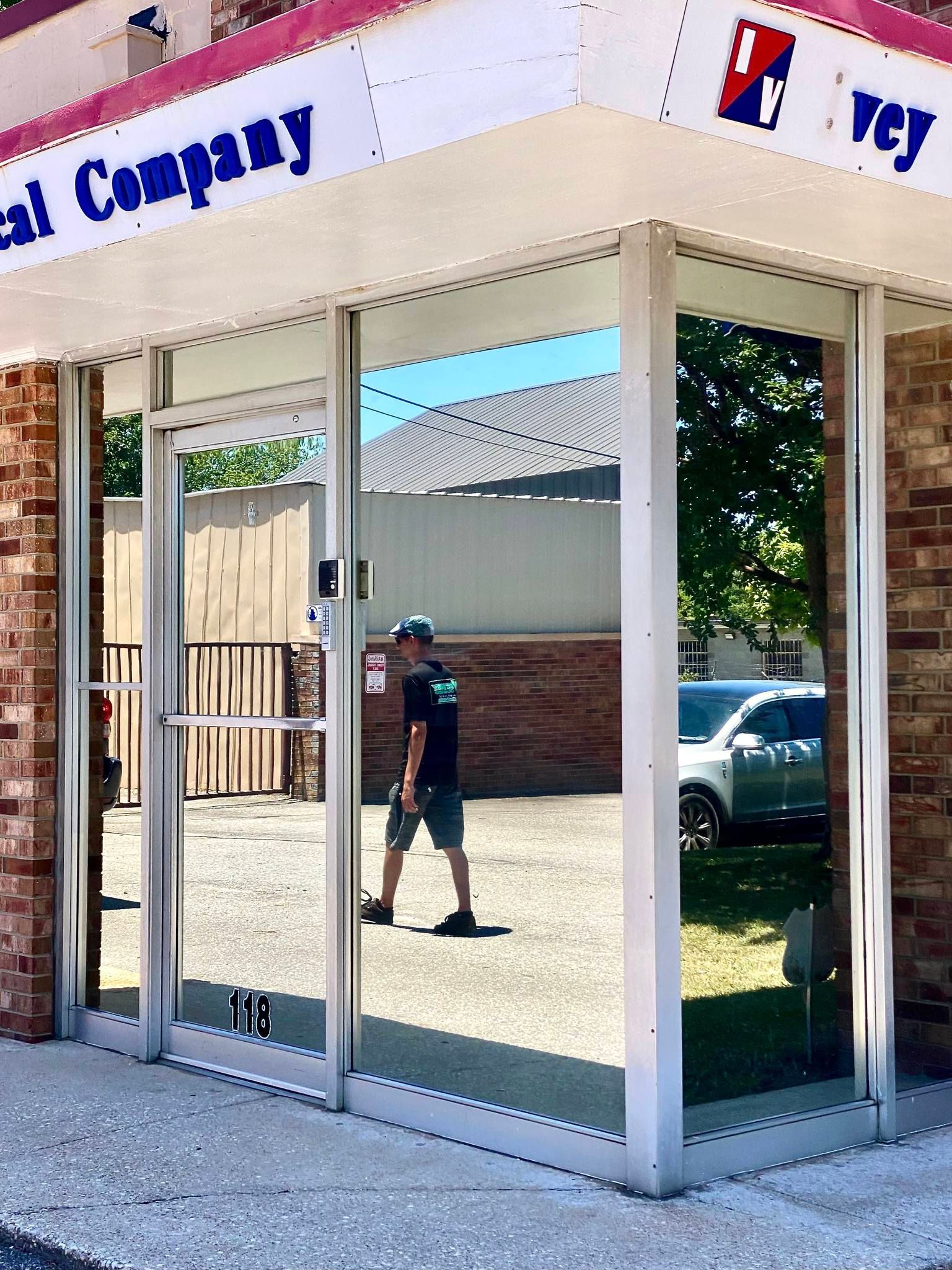 A person walking in front of a building entrance with reflective glass doors, a brick exterior, and a branded sign above.