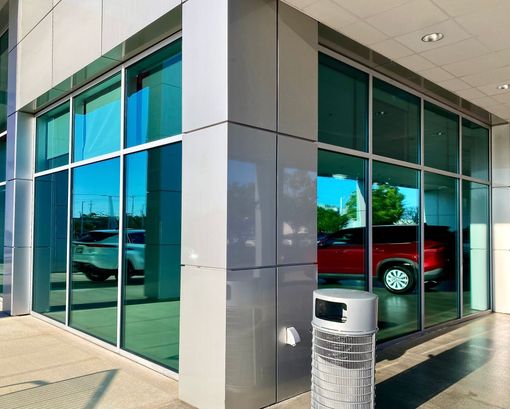 A modern commercial building corner with reflective glass windows showcasing a white car and a red SUV inside.