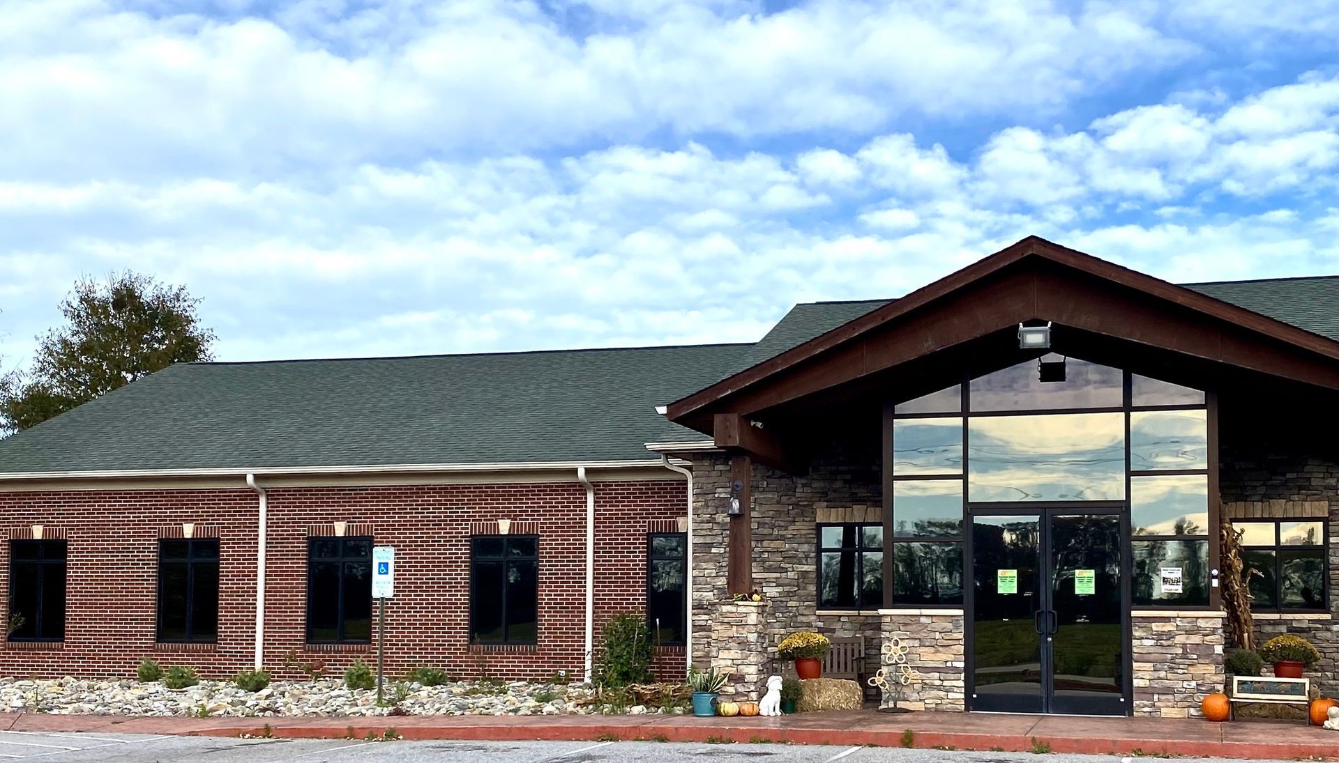 A single-story commercial building with red brick walls, stone accents, a dark shingled roof, and a glass-paneled entrance.