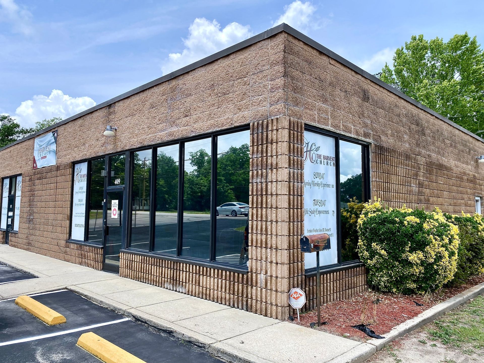 A single-story tan brick commercial building with large glass windows and an asphalt parking lot in front.