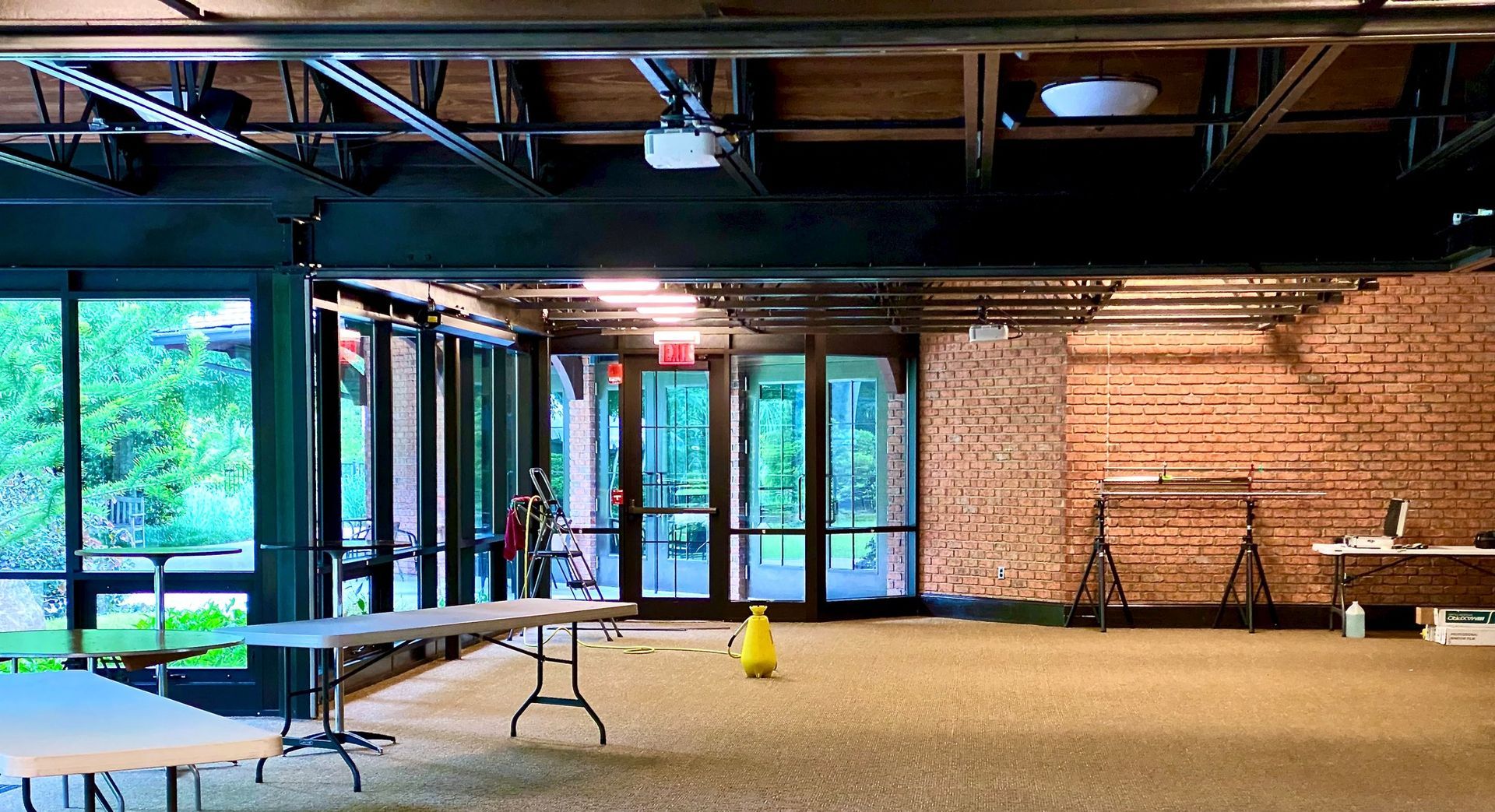 Interior of a modern space with brick walls, exposed ceiling, large windows, and folding tables set up for an event.