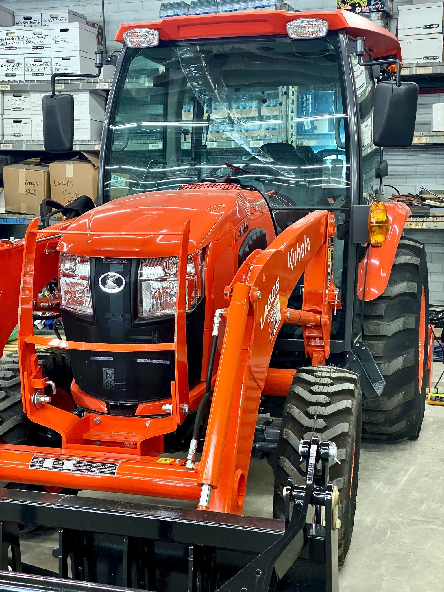 A bright orange Kubota tractor with a front loader and enclosed cabin, parked inside a warehouse storage area.