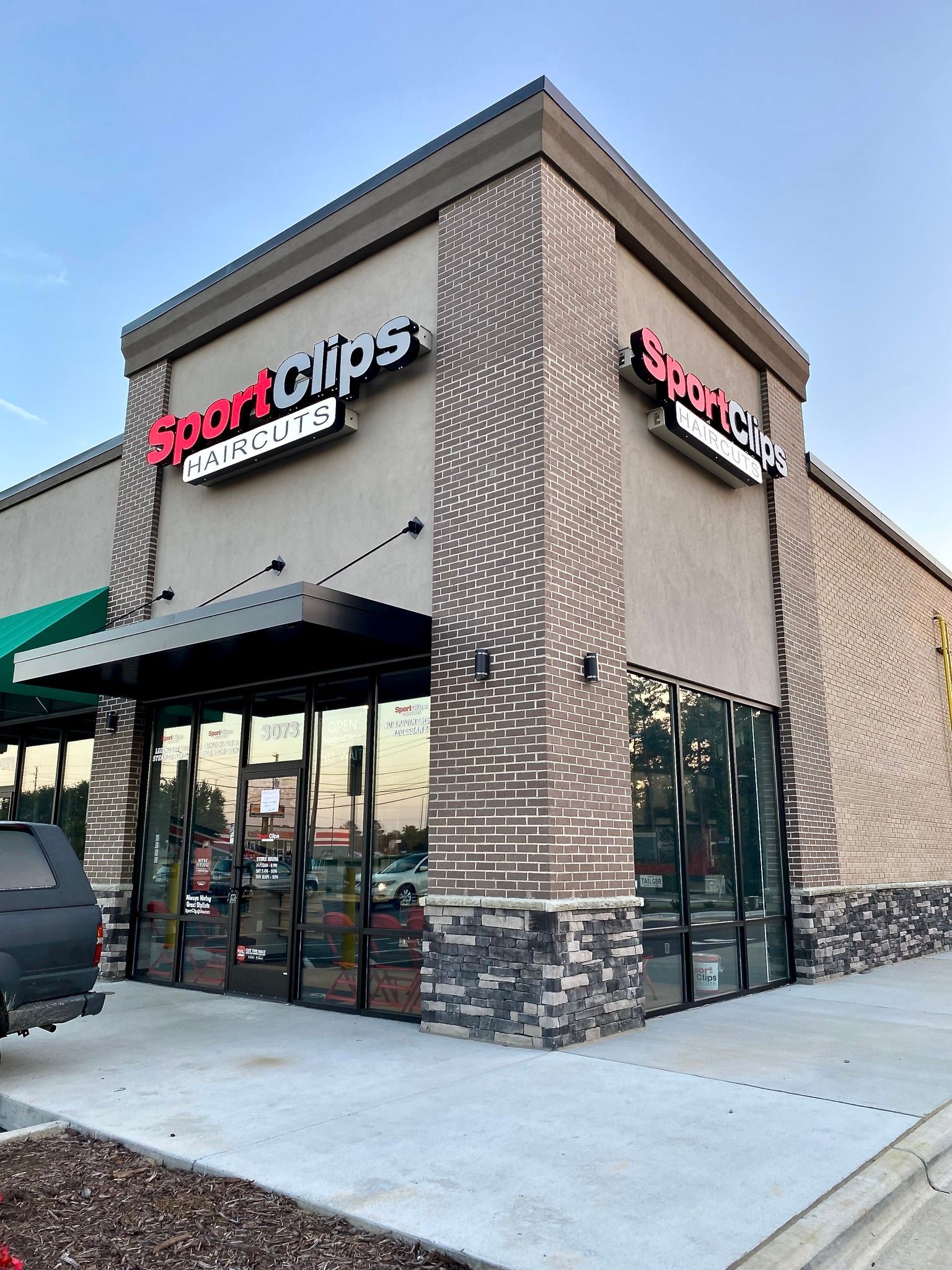 A corner storefront of a Sport Clips Haircuts, featuring beige stucco walls, dark stone trim, and large glass windows.