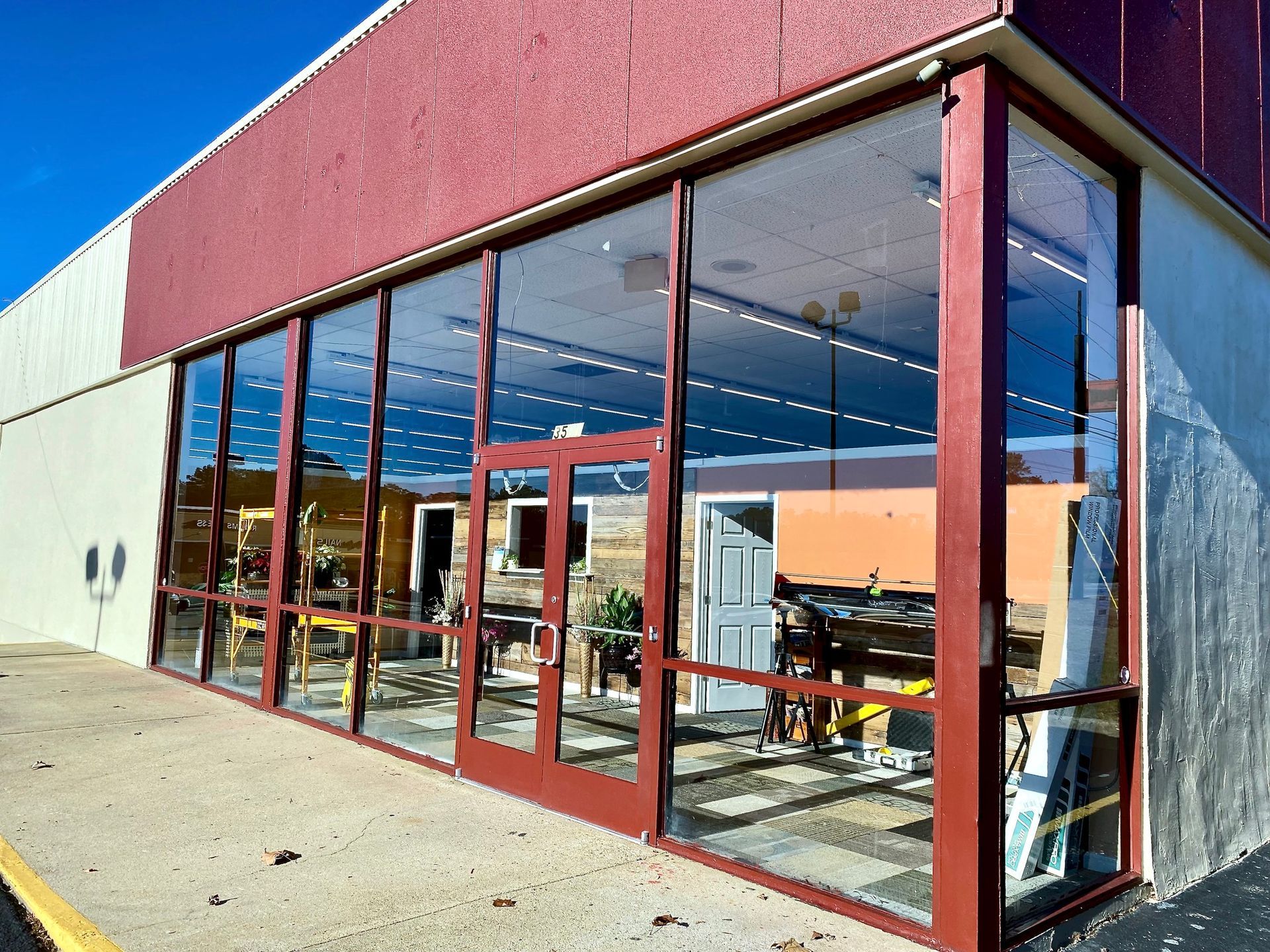 Exterior view of a commercial building with a red-framed glass storefront and double doors on a sunny day.