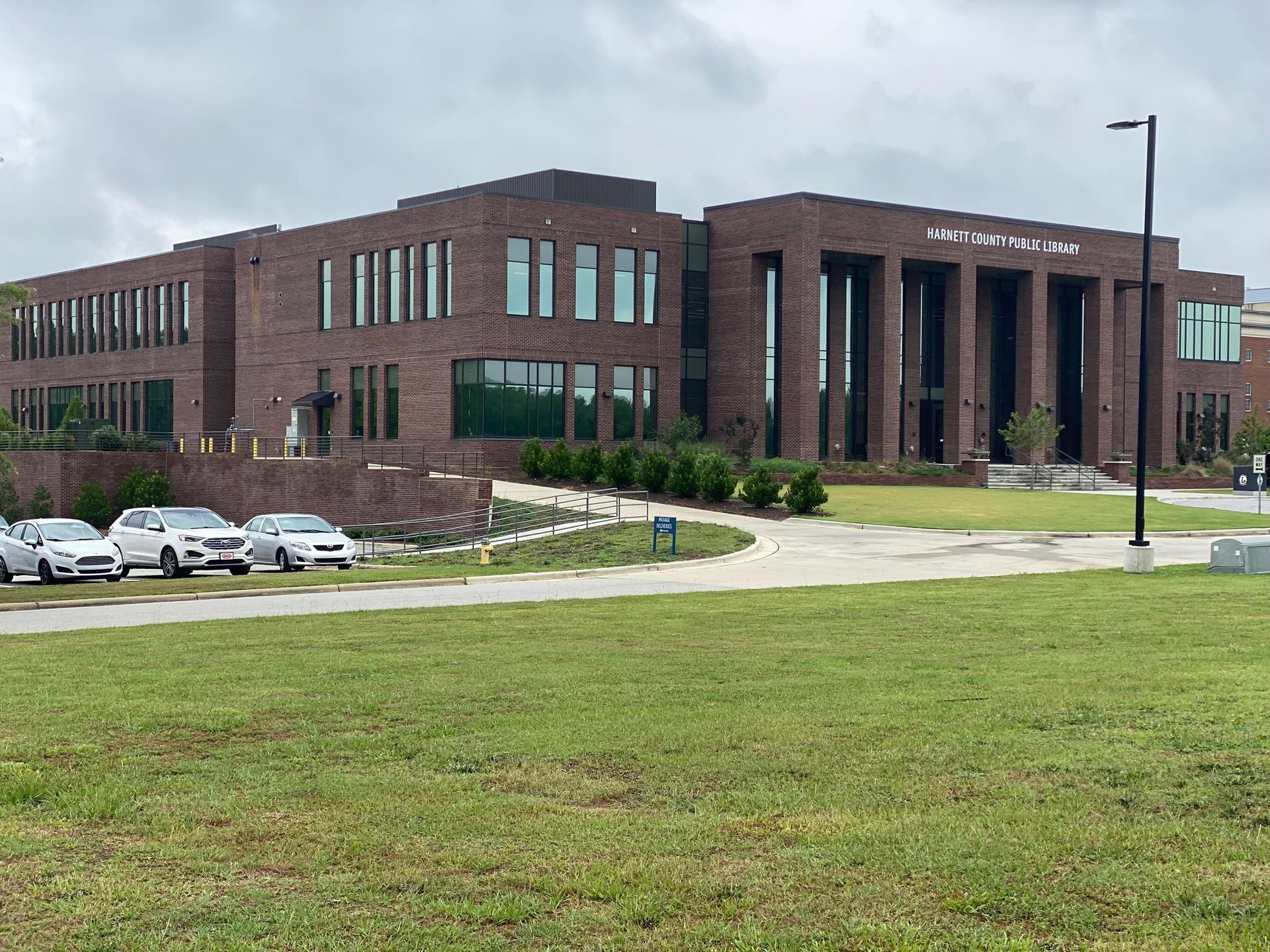 A modern, multi-story brick building with large glass windows and a prominent front entrance, viewed from a grassy lawn.