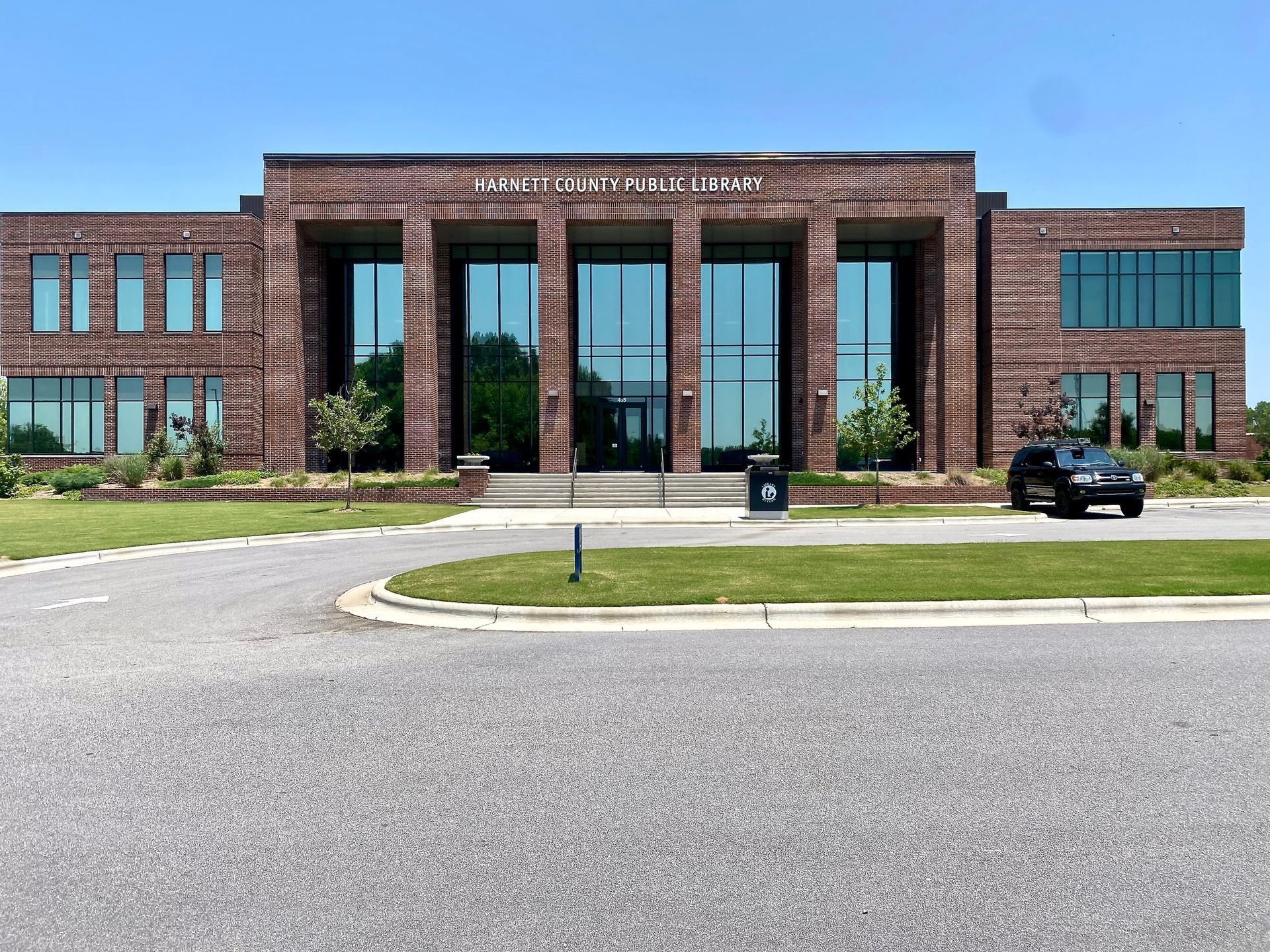 A modern two-story brick building with large glass windows and an entrance plaza, viewed across a parking lot.