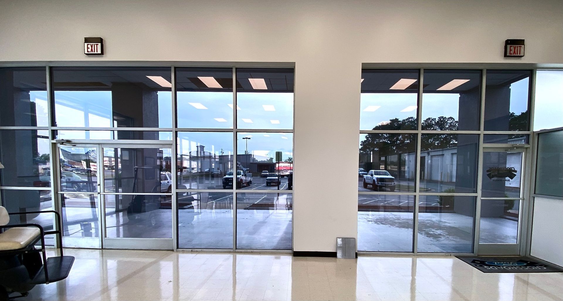 Two large glass-paned entrance doorways with metal frames leading to a parking lot under a cloudy sky.