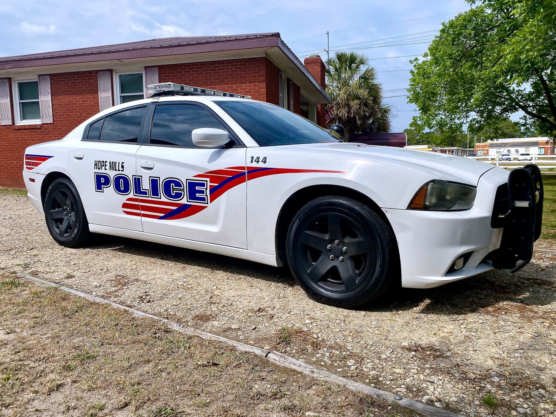 White Latelli police cruiser parked on a gravel lot in front of a red brick building.