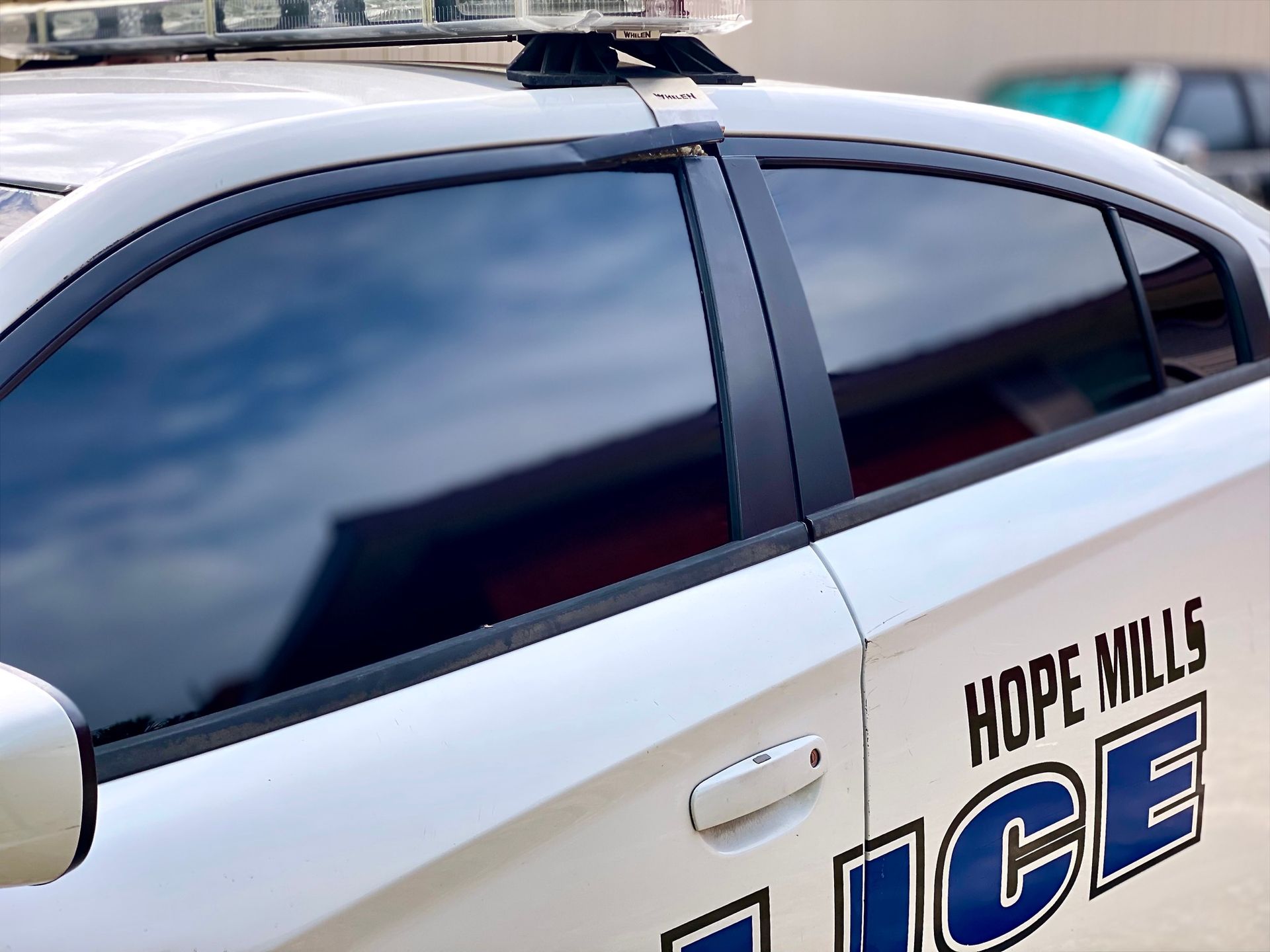 Side view of a white Hope Mills Police car showing a portion of the side windows and the department logo.