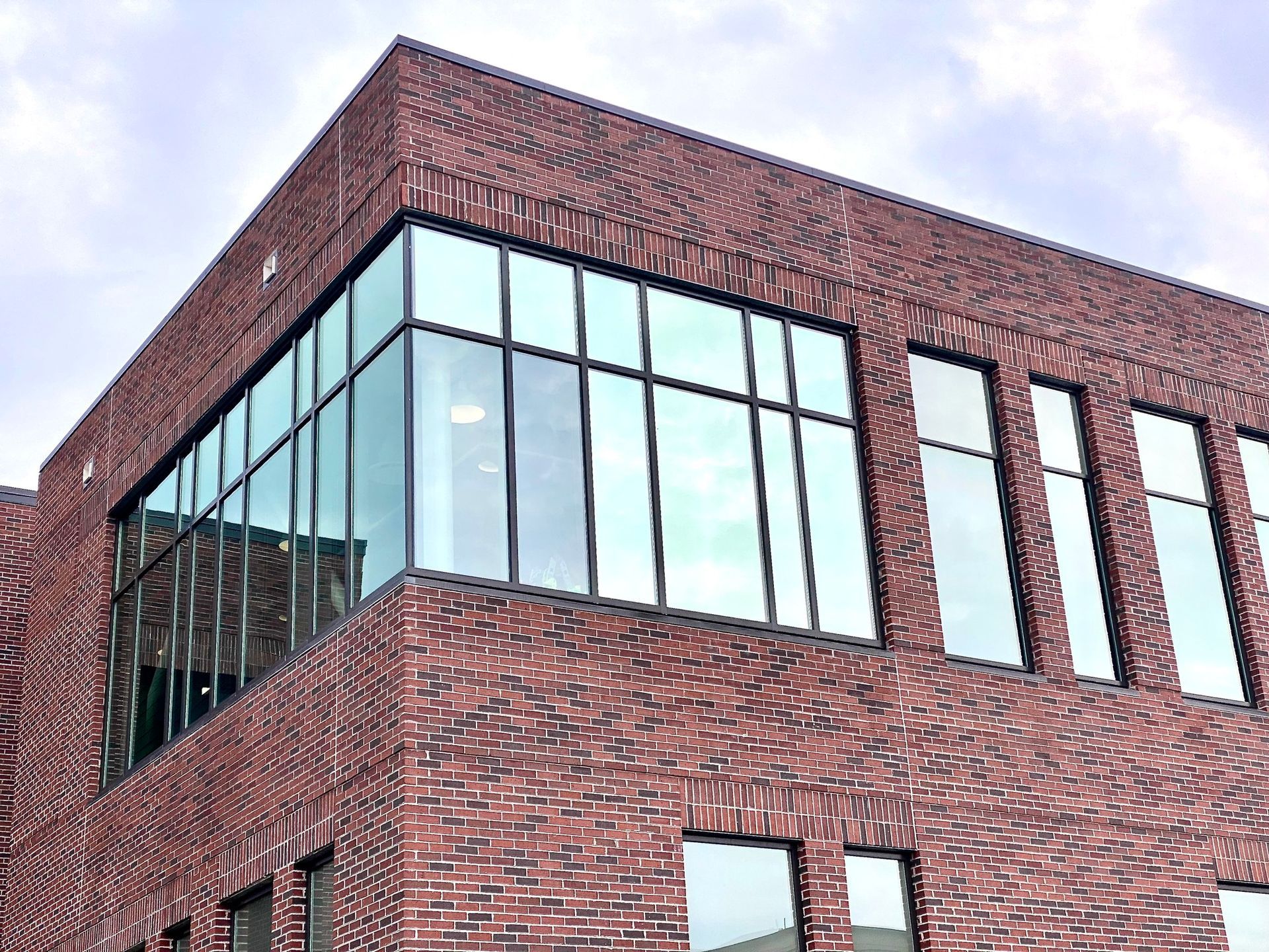 A corner view of a modern two-story building featuring dark red textured brickwork and expansive, floor-to-ceiling windows.