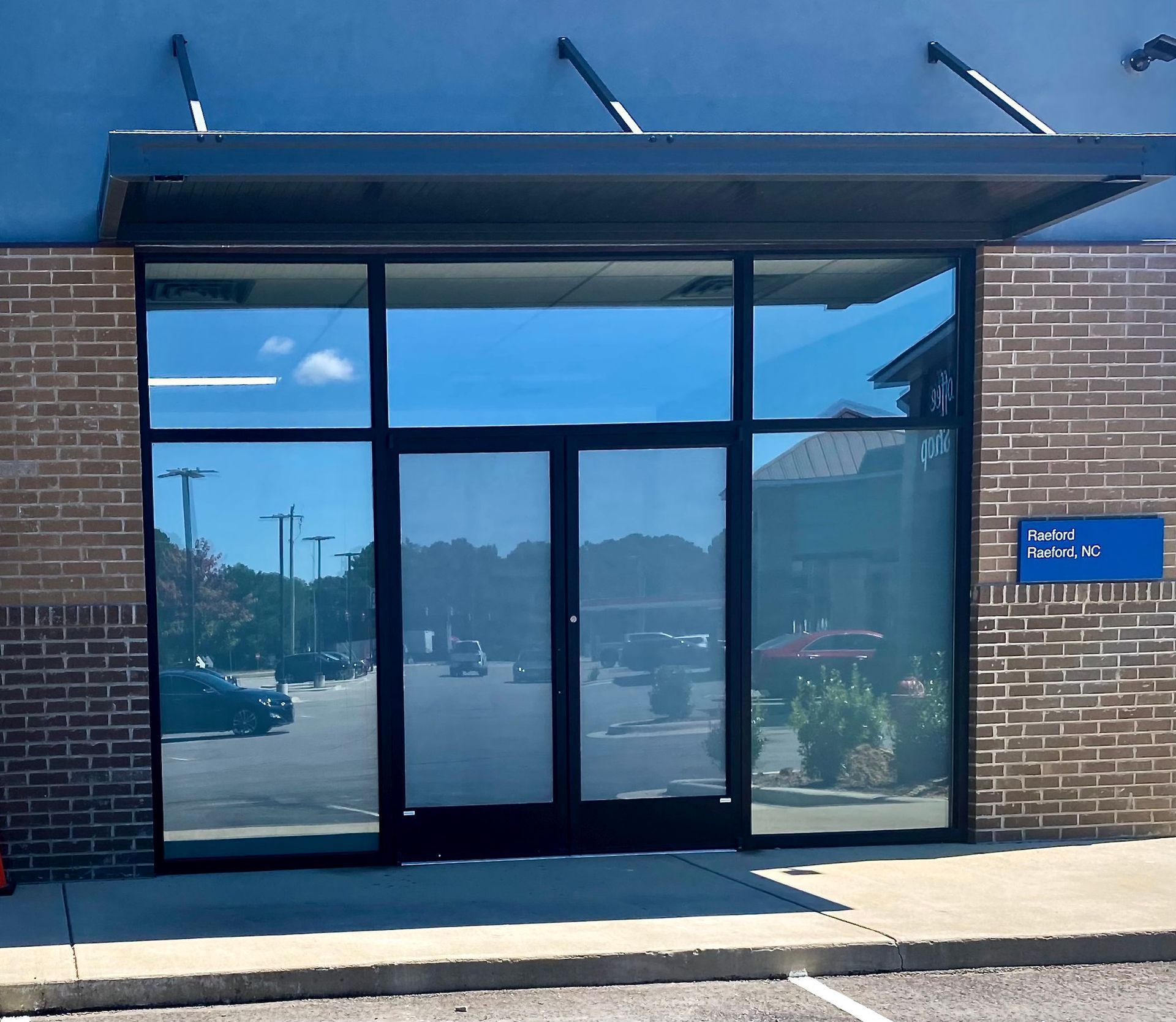An exterior view of a commercial building entrance with brick walls, a dark metal awning, and reflective glass doors.