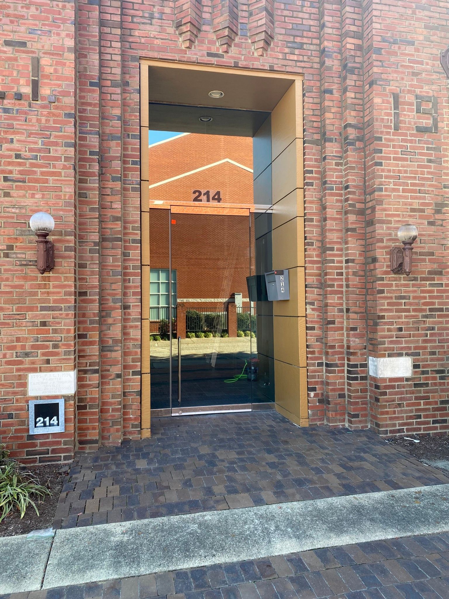 Entrance to a brick building with the number 214 above the glass doorway, which reflects another brick building outside.