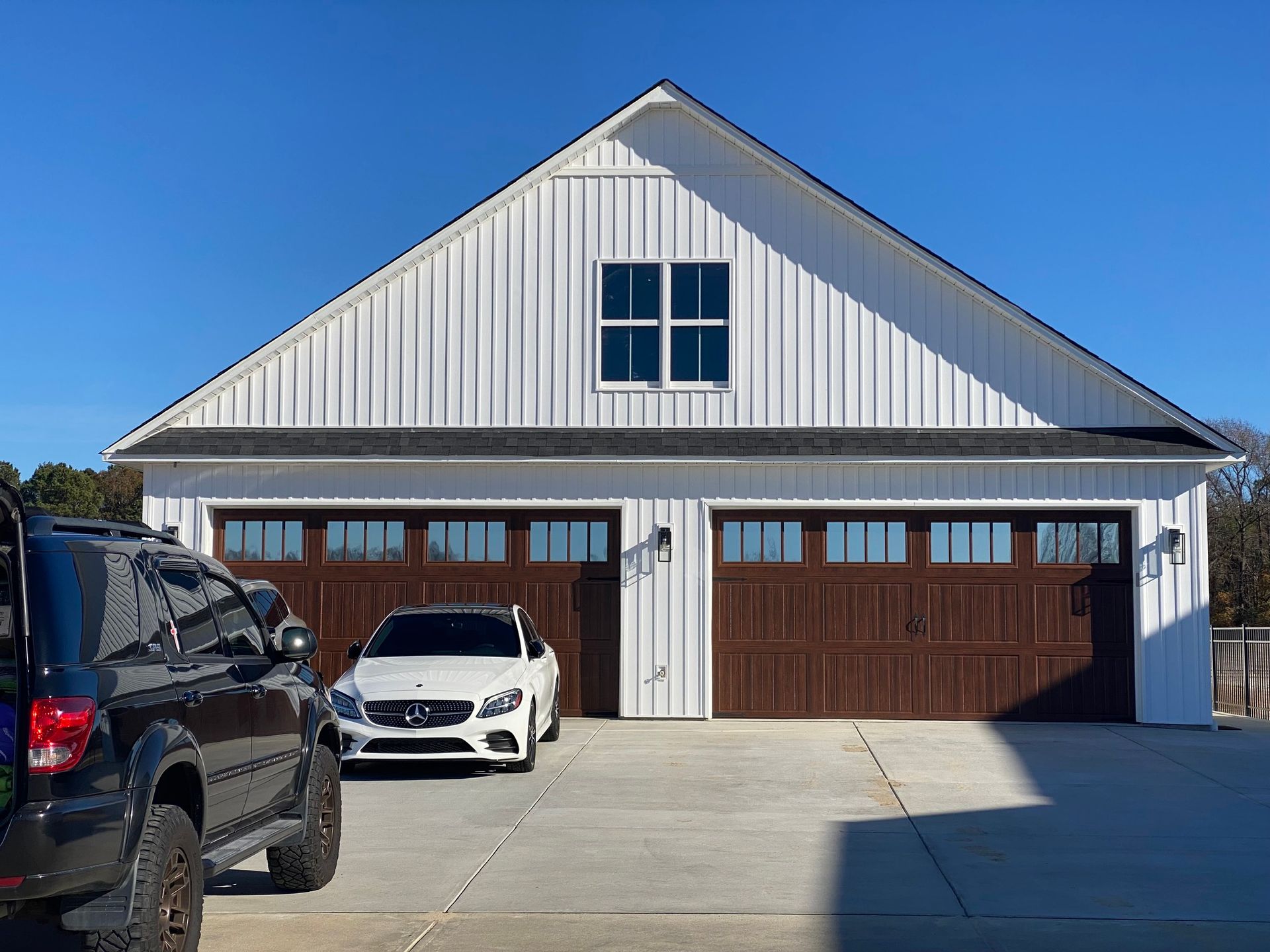 A white board-and-batten garage with two dark brown carriage-style doors and a centered window under a blue sky.