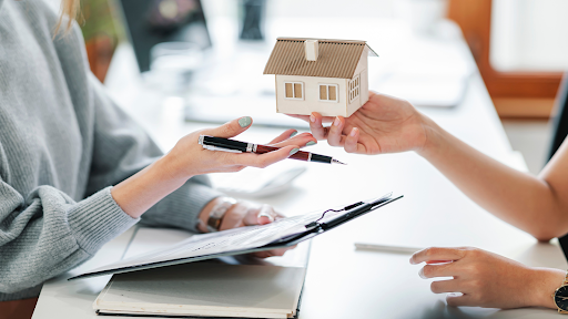 A woman is holding a model house in her hand while sitting at a table.