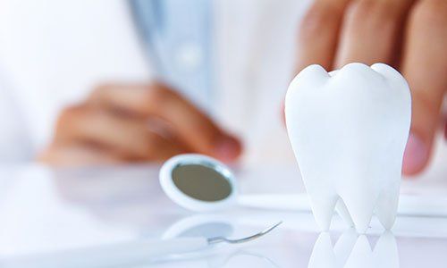 un dente in ceramica, uno specchietto e dietro l’immagine sbiadita di due mani di un dentista con il camice bianco