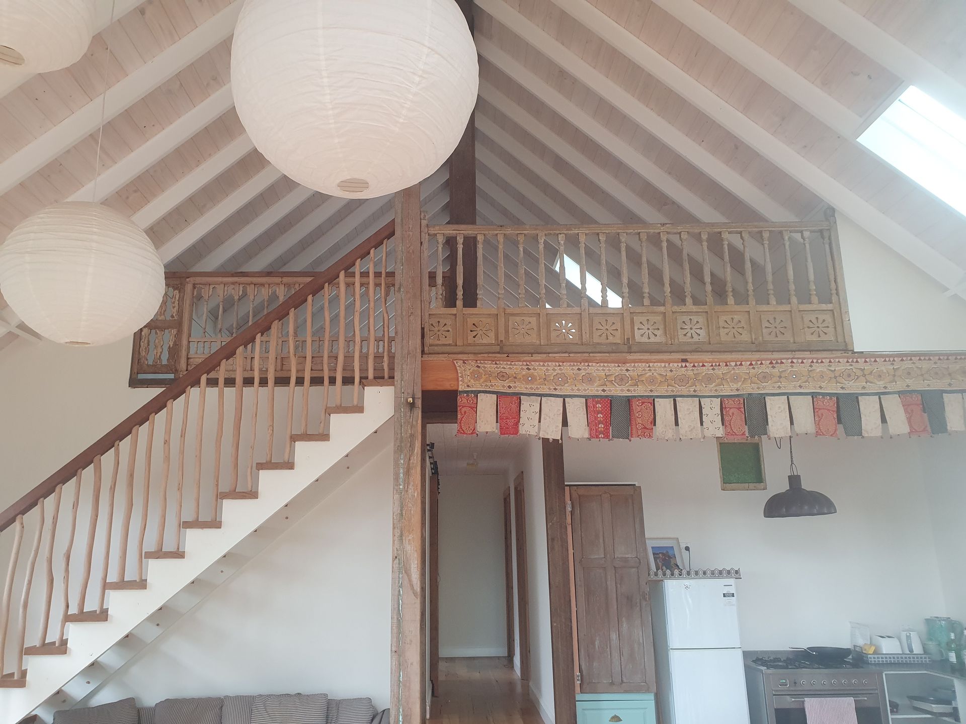 Interior with staircase leading to a balcony, featuring white walls, paper lanterns, and wooden accents.