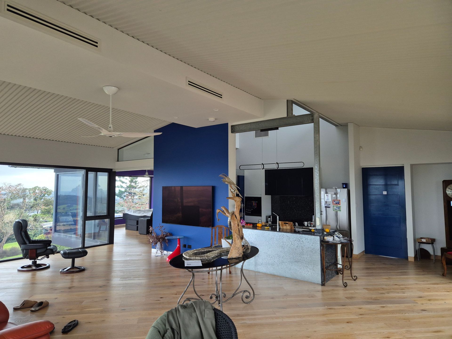 Spacious room with wood floors, blue accent wall, and a view through large windows.
