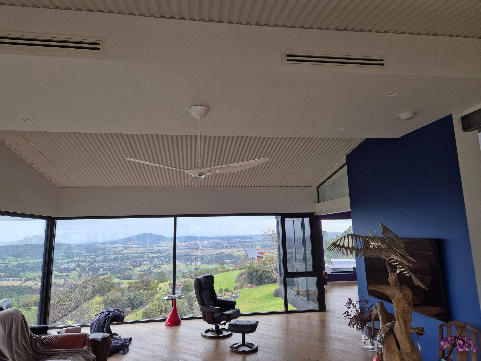 Living room with large windows overlooking a green landscape. White ceiling fan, leather chair, blue wall.