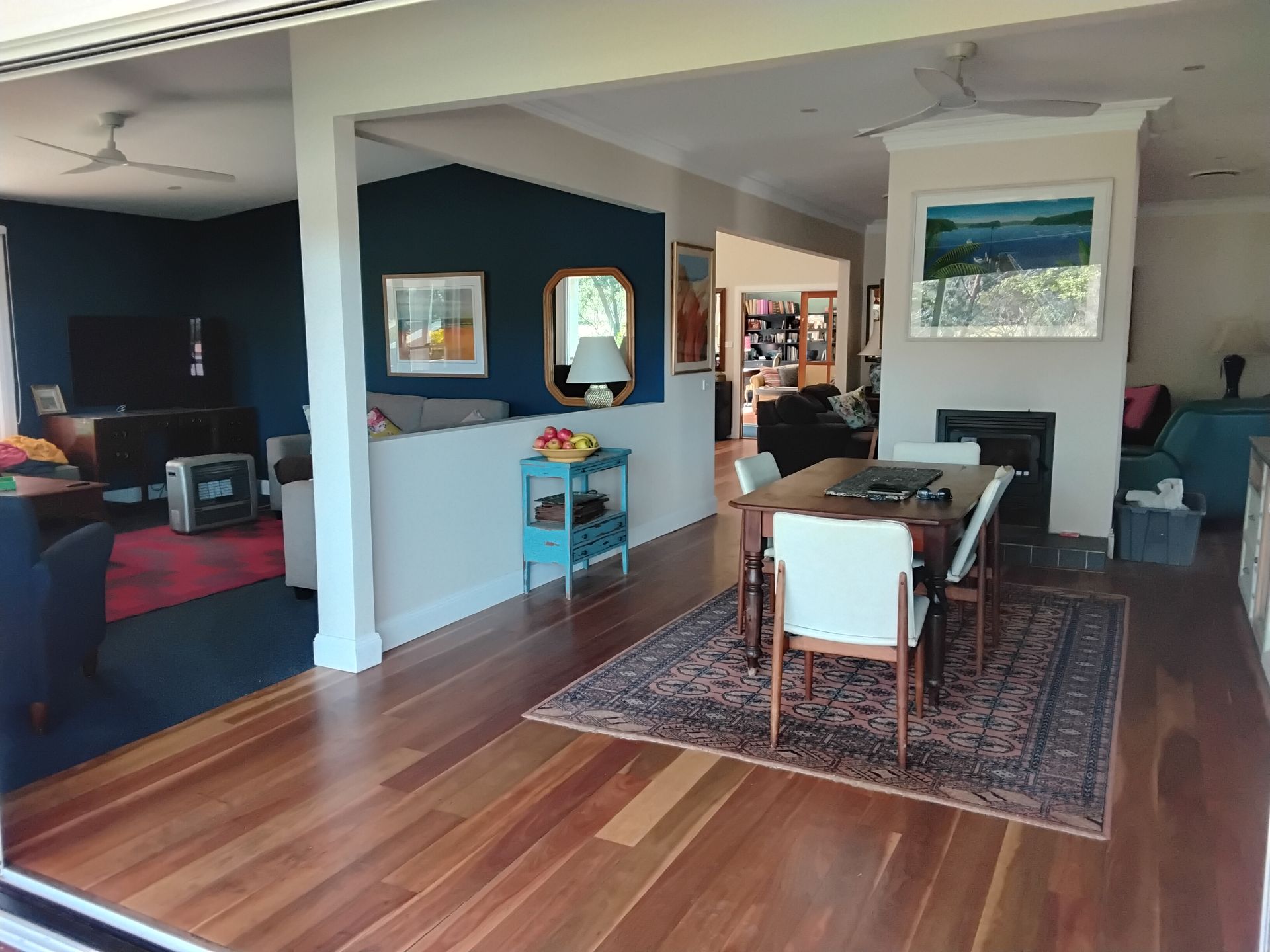Spacious home interior with dark blue accent wall, hardwood floors, dining area with Persian rug, and living room visible.