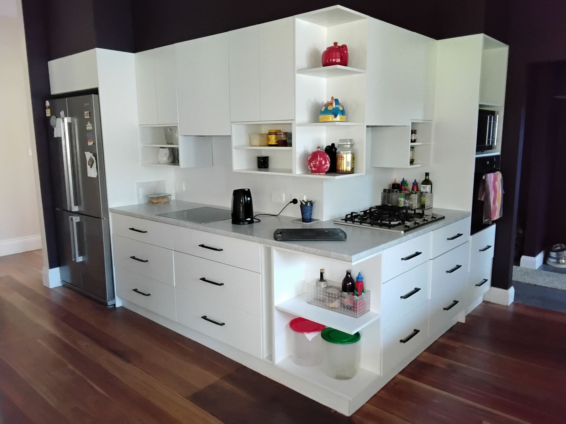 White modern kitchen with stainless steel fridge, cooktop, and storage cabinets.