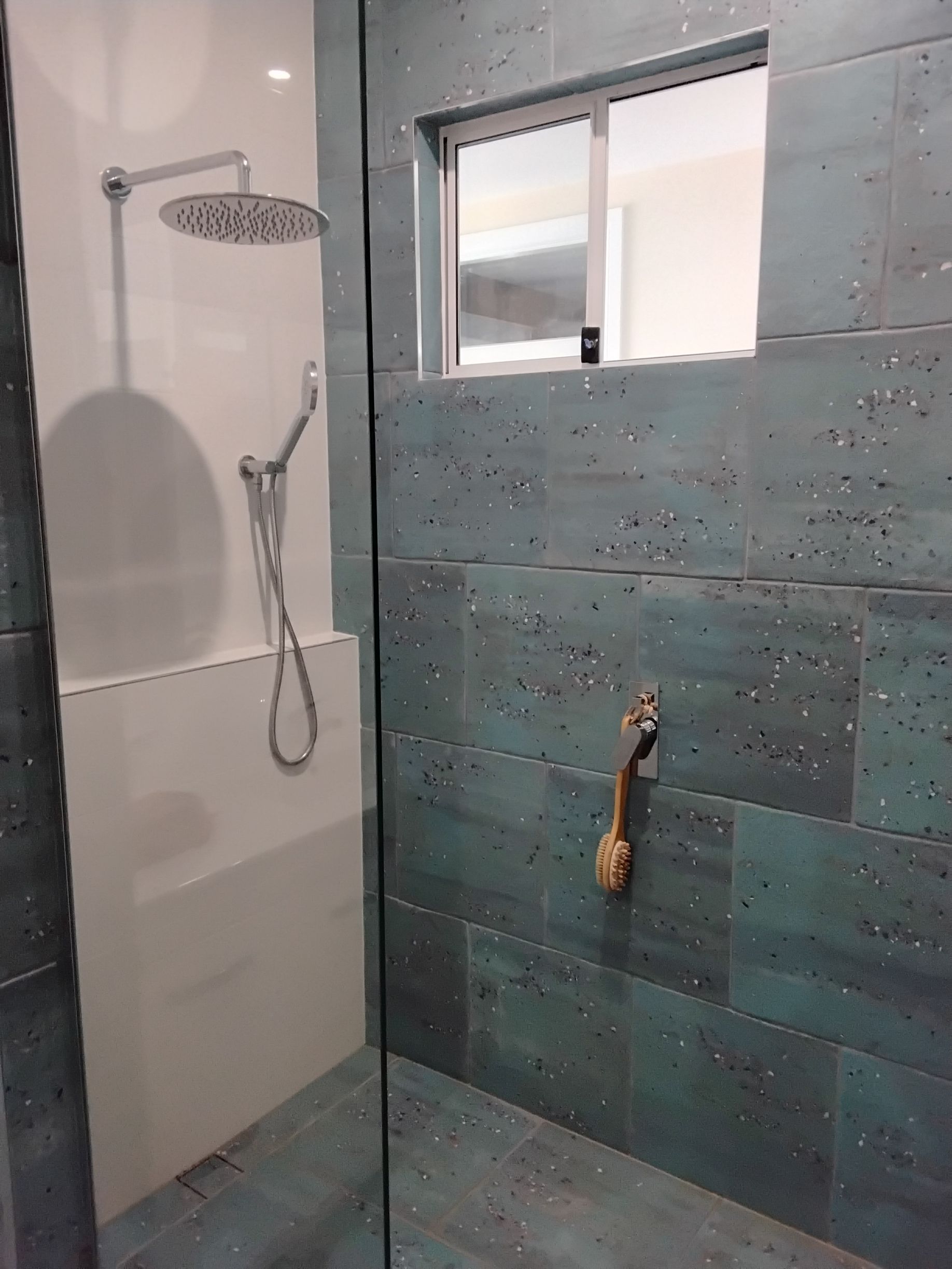 Shower with teal-green tile, a glass door, and a white showerhead fixture.