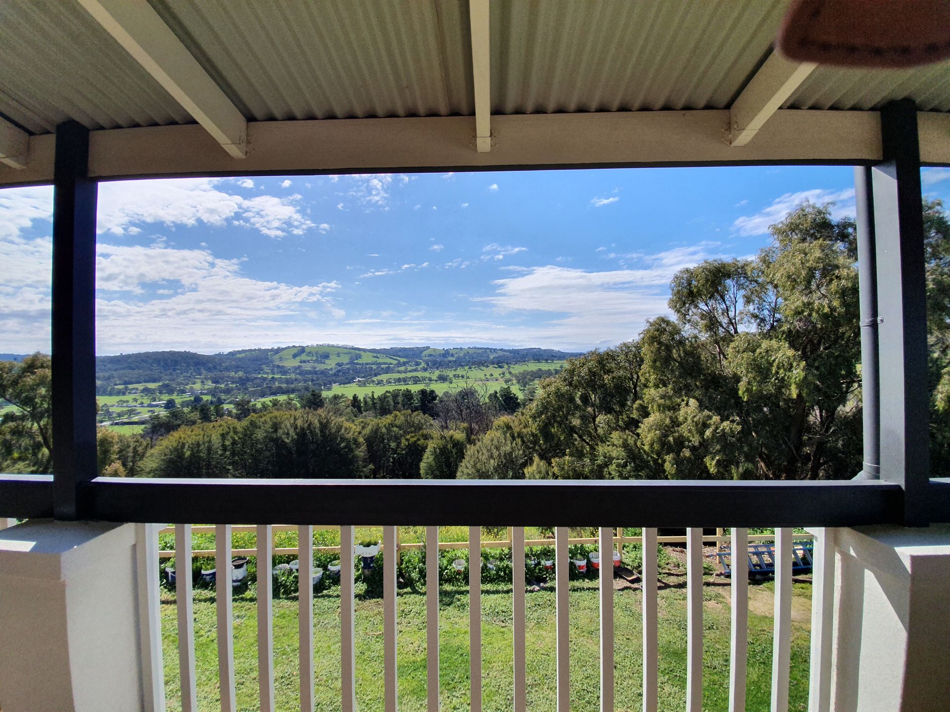 View of green valley, trees, and blue sky from a balcony with white railing and black trim.