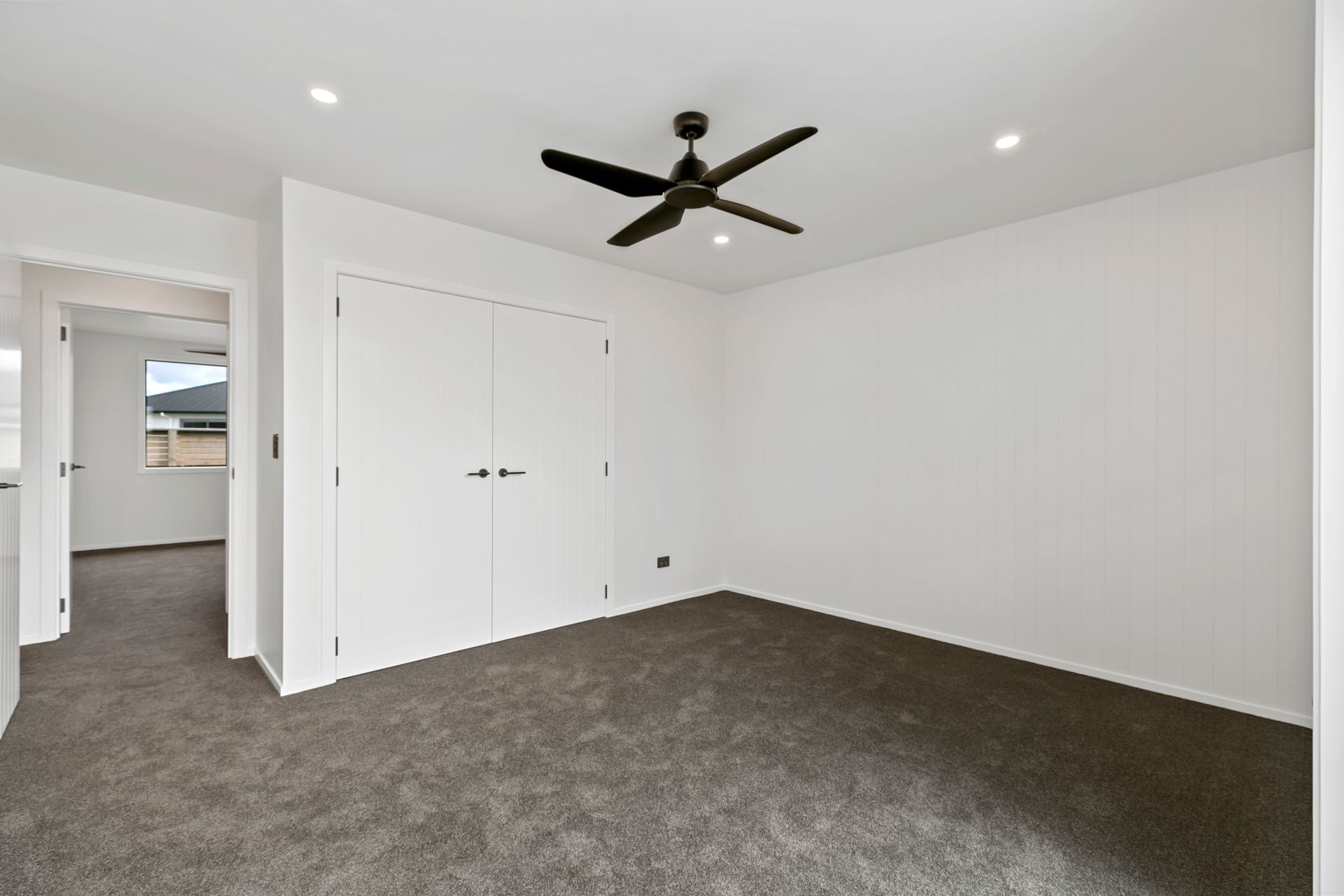 Empty bedroom with white walls, dark gray carpet, and a ceiling fan.